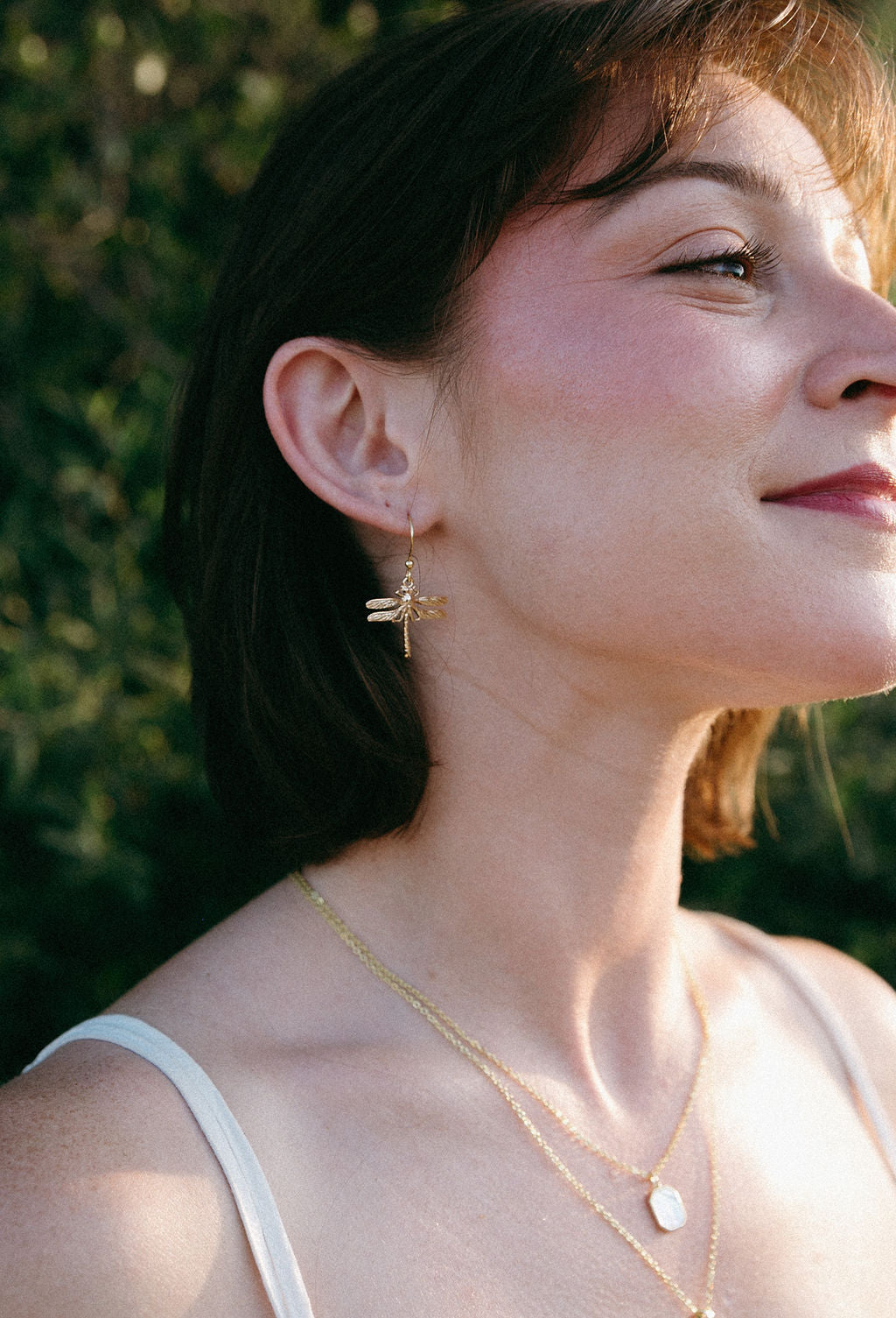 Gold dragonfly drop earrings worn on ear, delicate minimalist jewelry styling