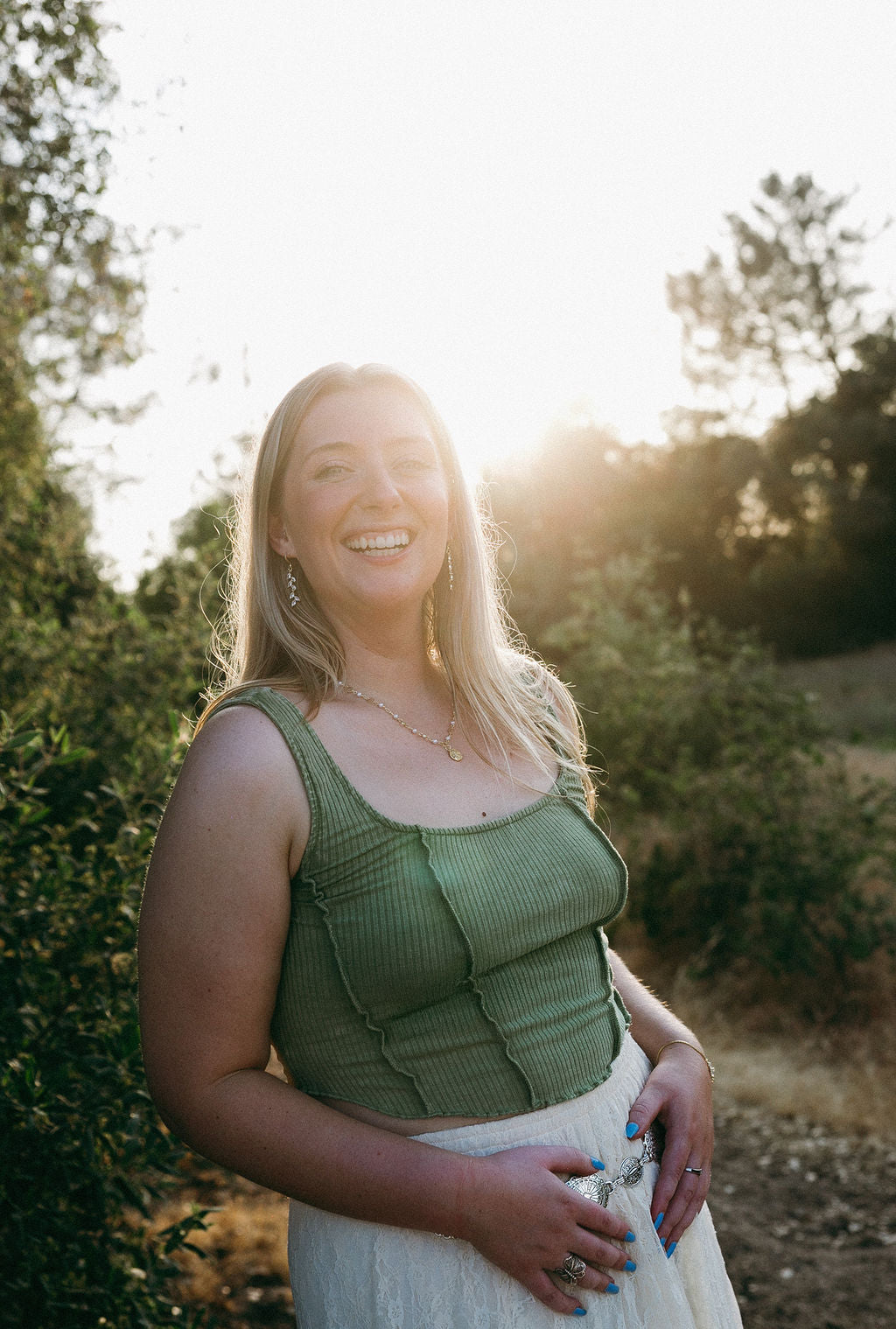 Woman wearing gold leaf drop earrings in golden hour light, soft feminine jewelry style
