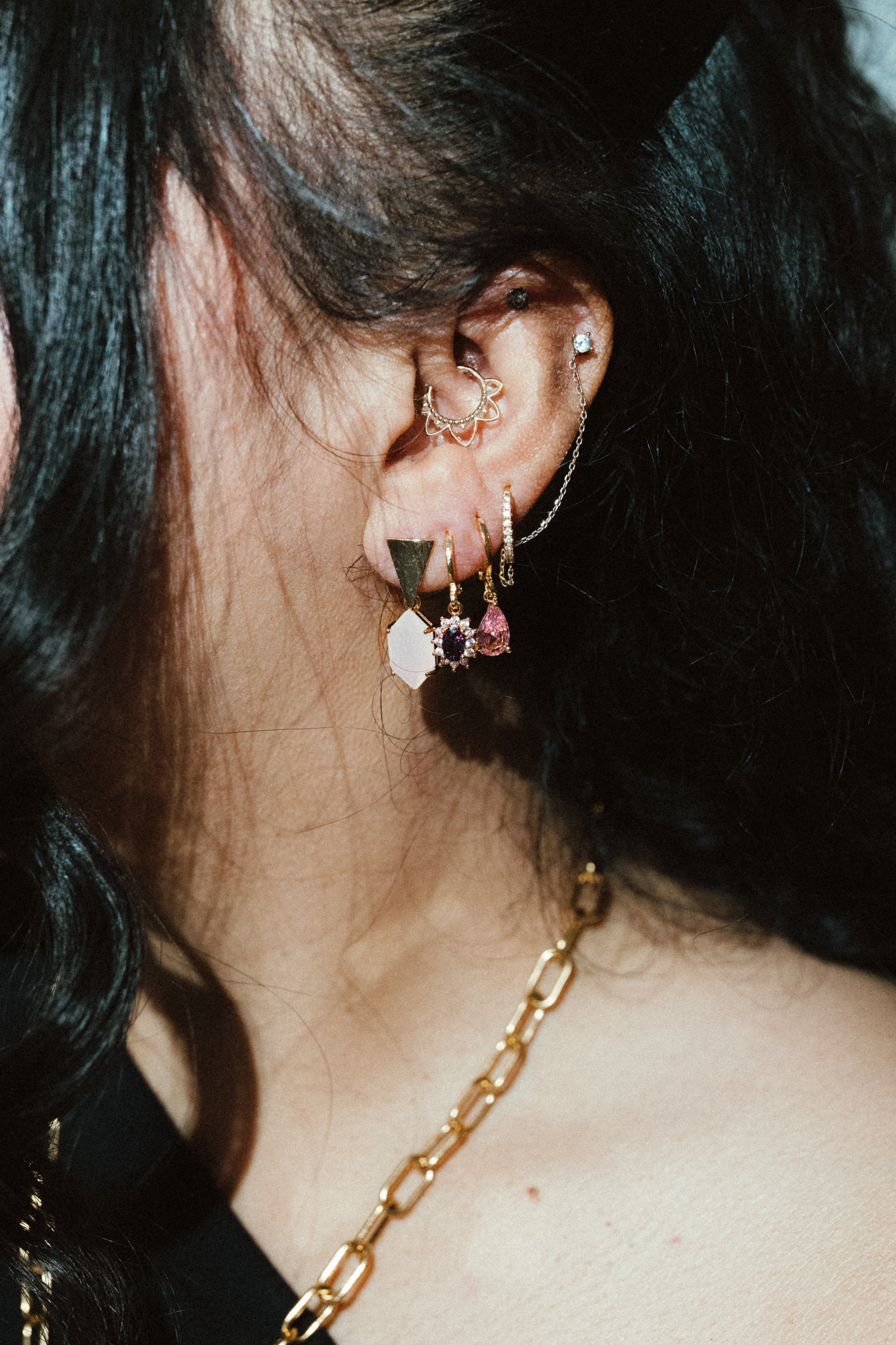 Gold huggie earrings styled in ear stack with mixed charms, trendy layered jewelry look