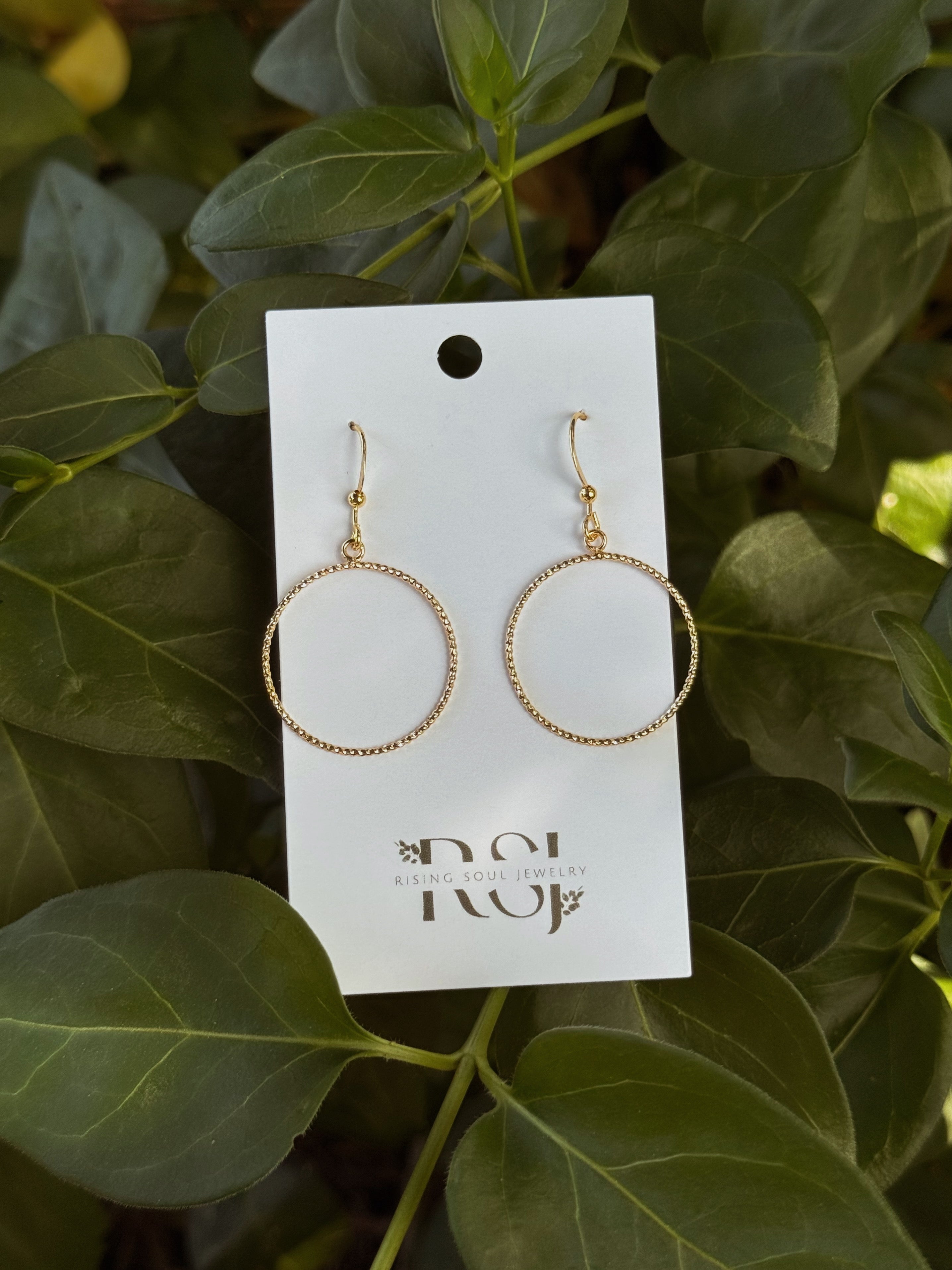 Gold circle hoop earrings displayed on jewelry card with greenery background, earthy aesthetic jewelry