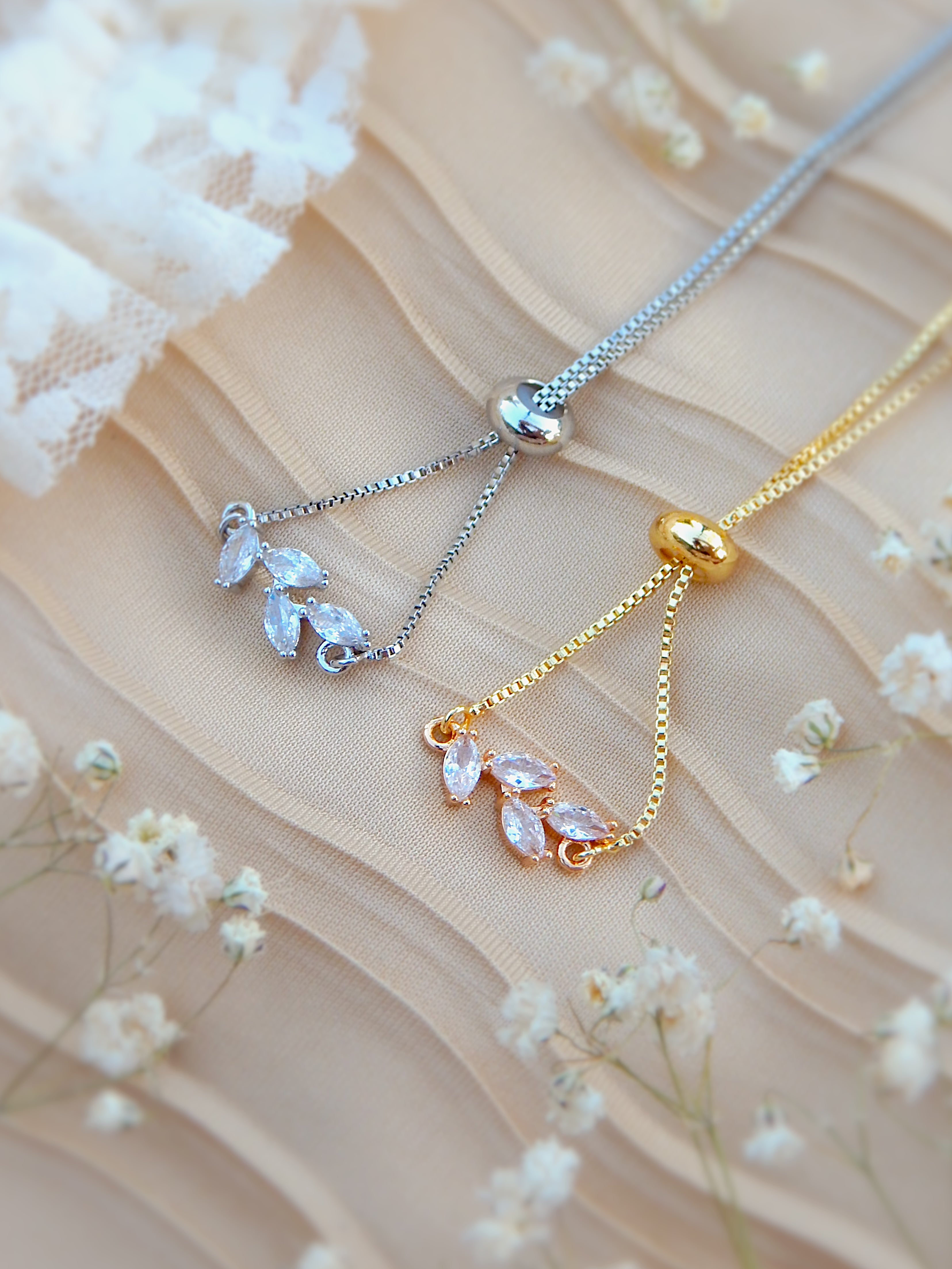 Gold and silver bloom bracelets with floral charm details on neutral background with flowers
