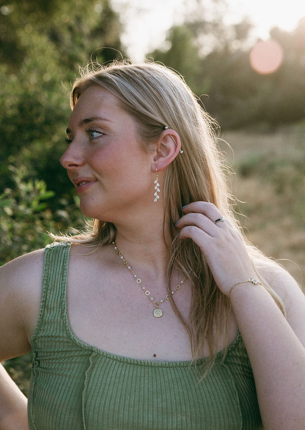 Dainty gold leaf dangle earrings worn on ear, nature inspired jewelry styled outdoors