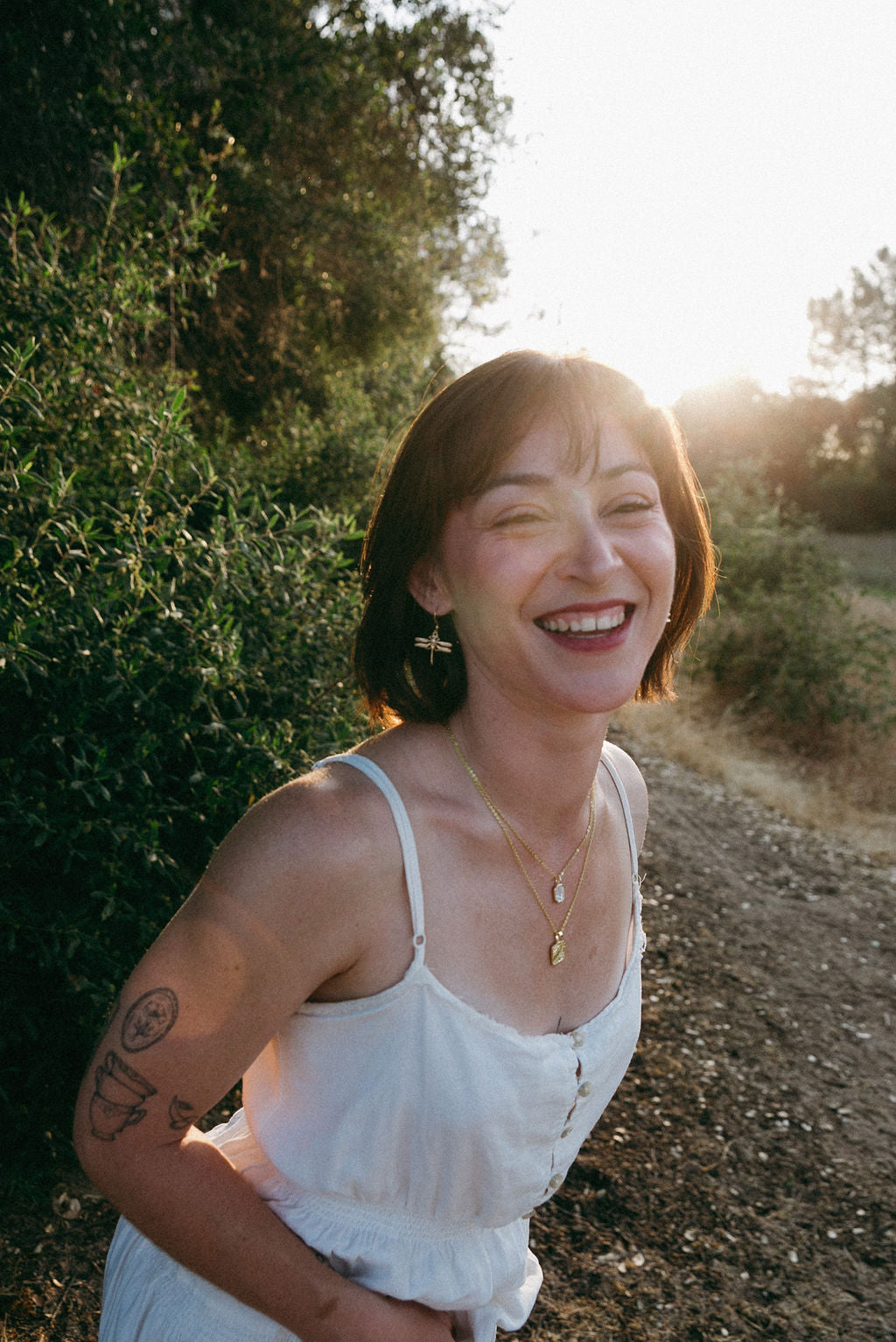 Woman wearing gold dragonfly earrings in sunlight, soft feminine jewelry aesthetic