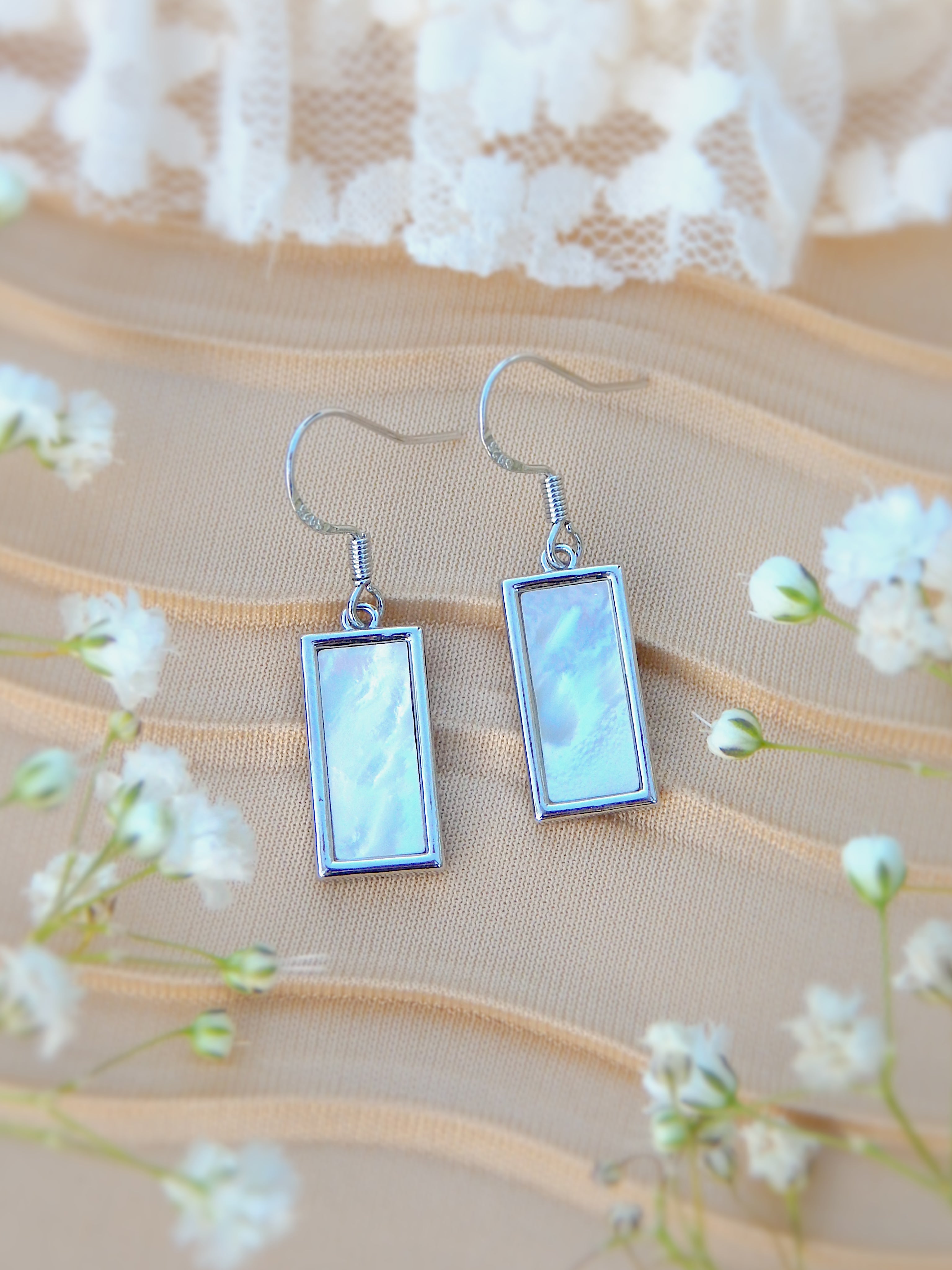 Silver rectangle earrings with mother of pearl inlay displayed on soft neutral background with delicate floral accents