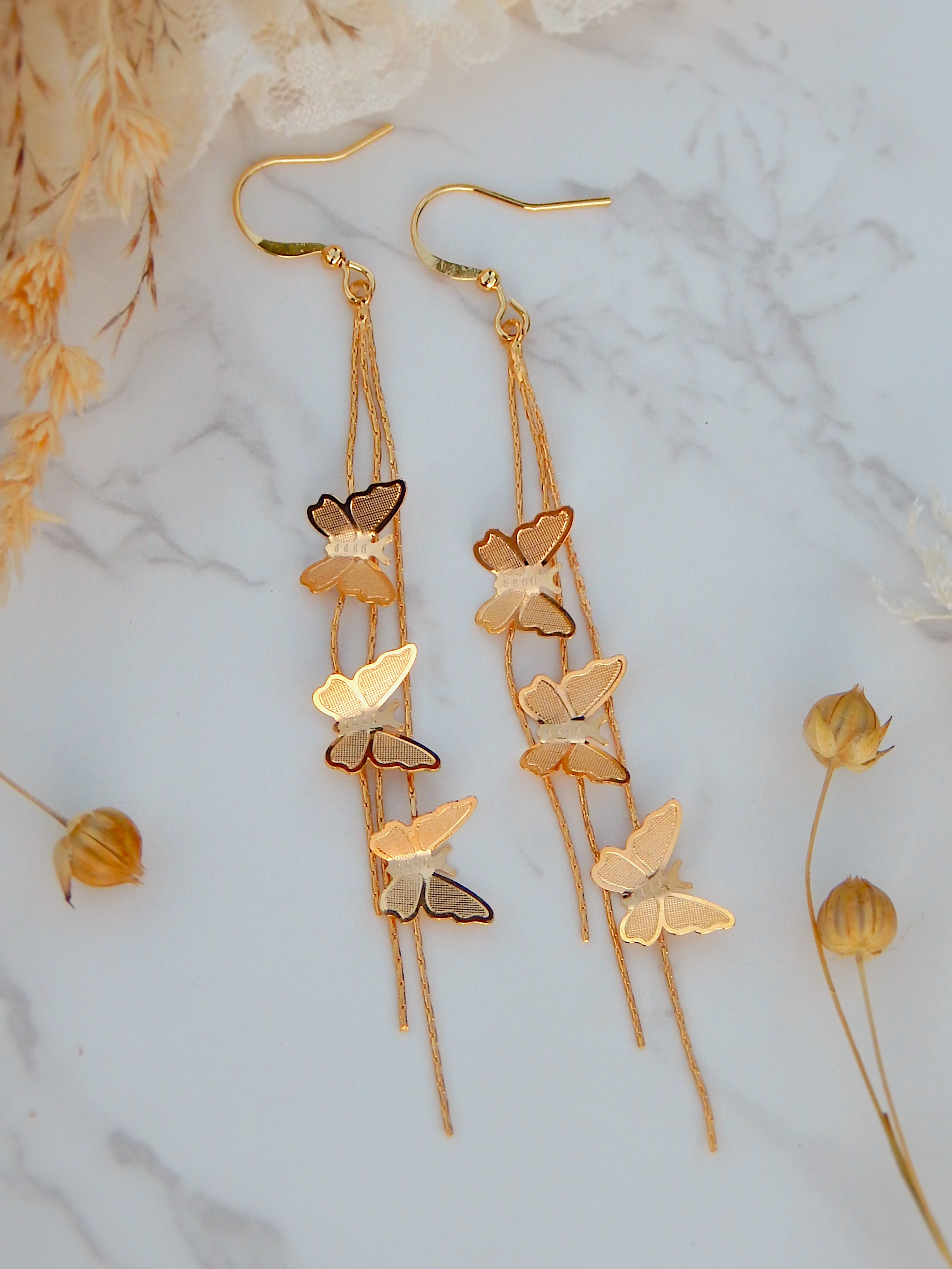 Gold cascading butterfly drop earrings with delicate chain details on marble background