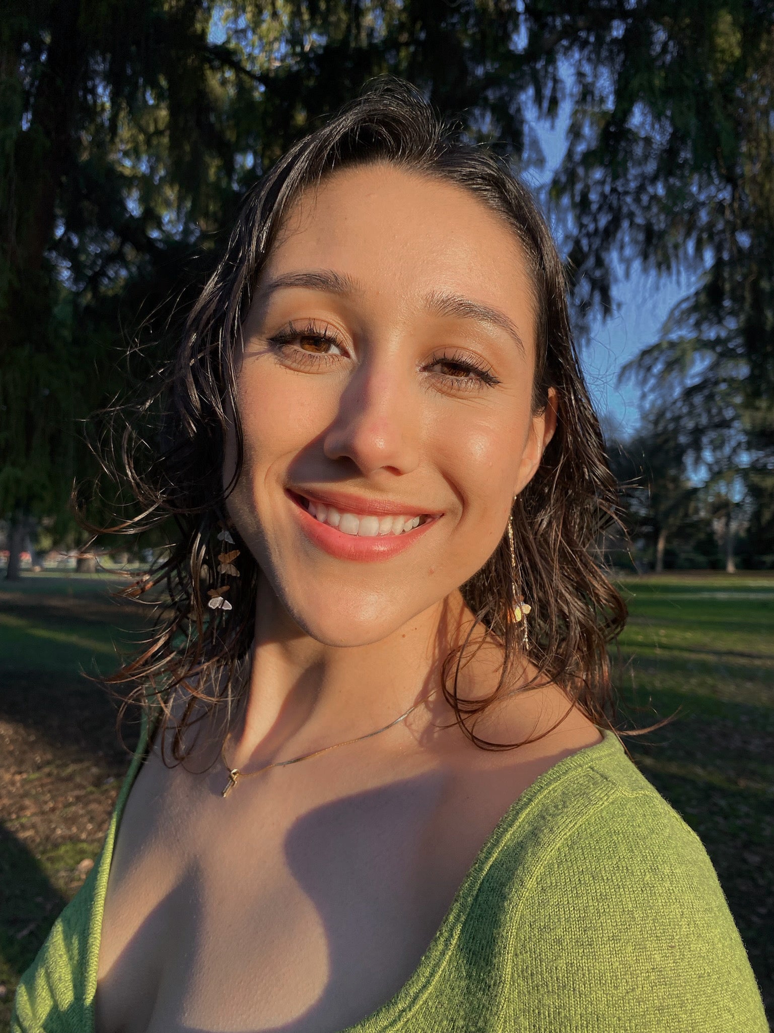 Smiling woman wearing gold butterfly drop earrings in soft golden hour lighting