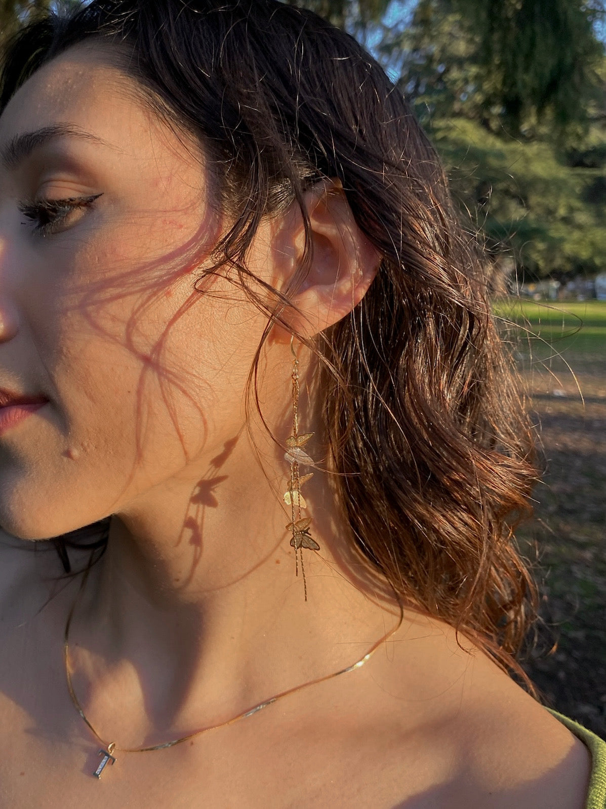 Woman wearing gold butterfly drop earrings with cascading chains in warm natural light