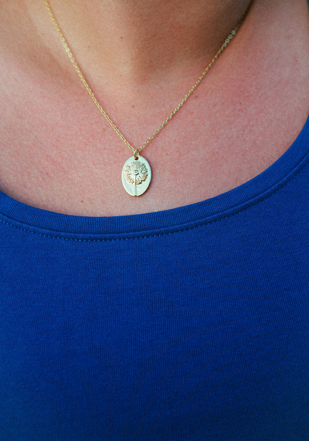 Gold dandelion wish necklace worn on neck, delicate engraved pendant styled for everyday wear