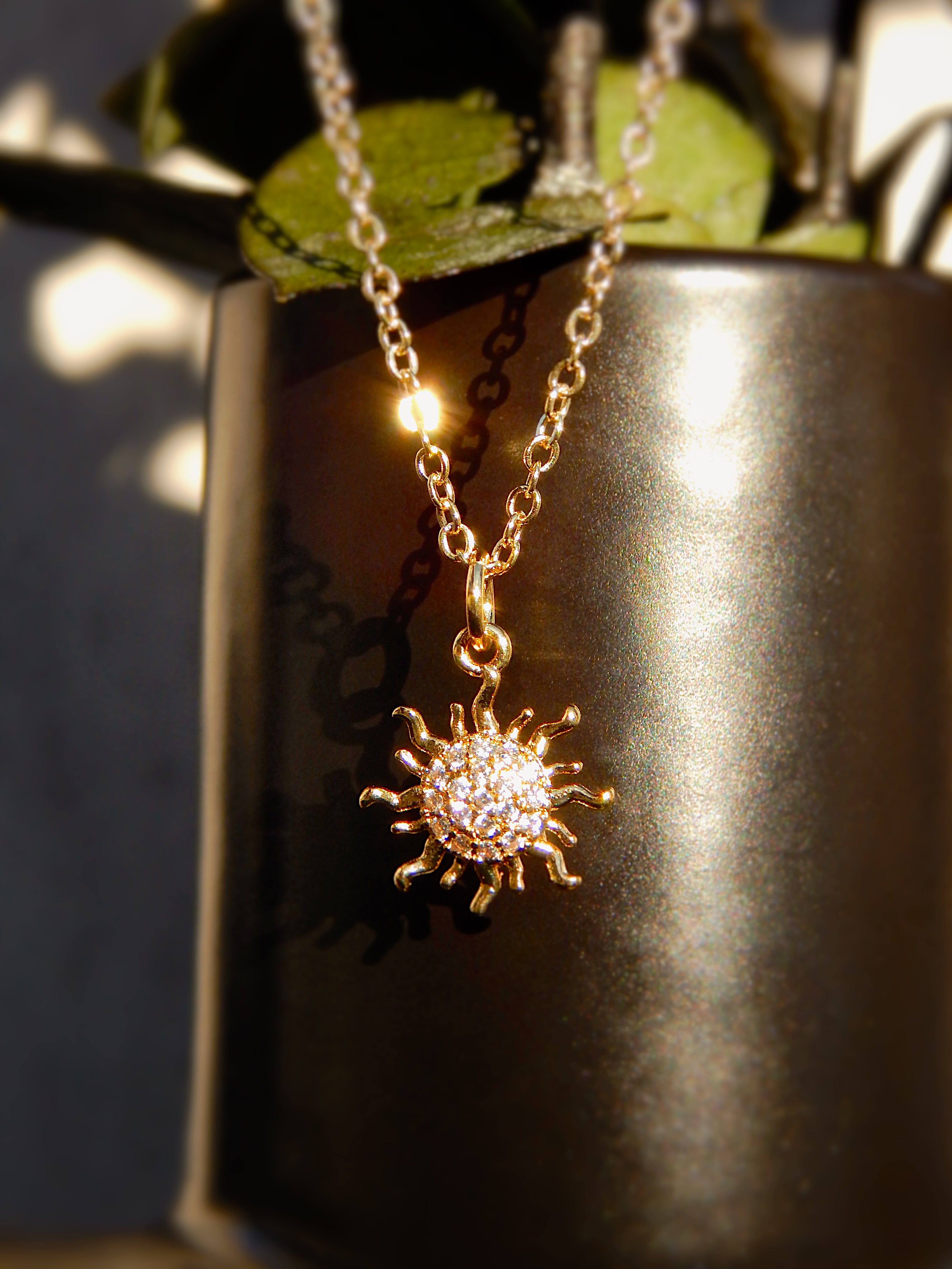 Dawn Necklace displayed in warm golden sunlight, highlighting the sparkling cubic zirconia sun pendant.