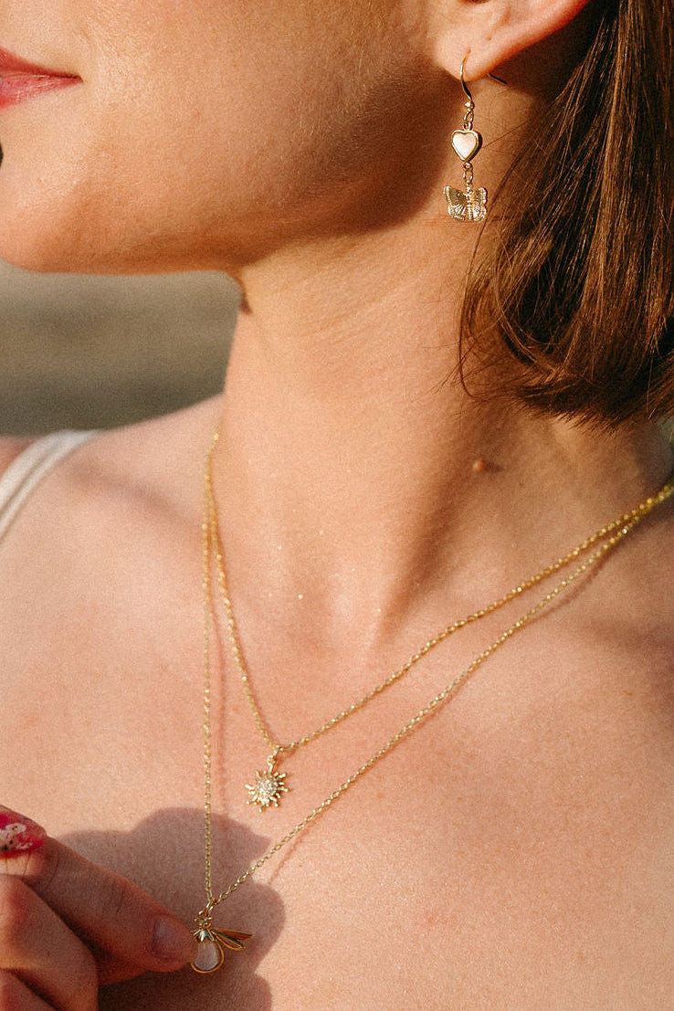 Model wearing the Dawn Necklace, a dainty gold sun pendant necklace, layered with other gold necklaces.