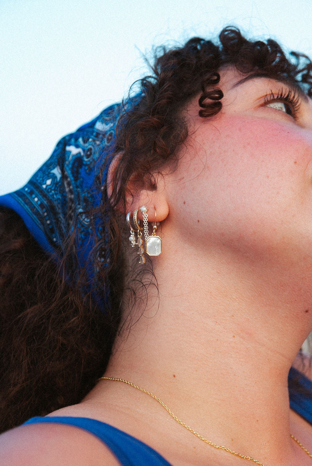 Close-up of woman wearing gold mother of pearl drop earrings in octagon shape, minimal everyday jewelry styling