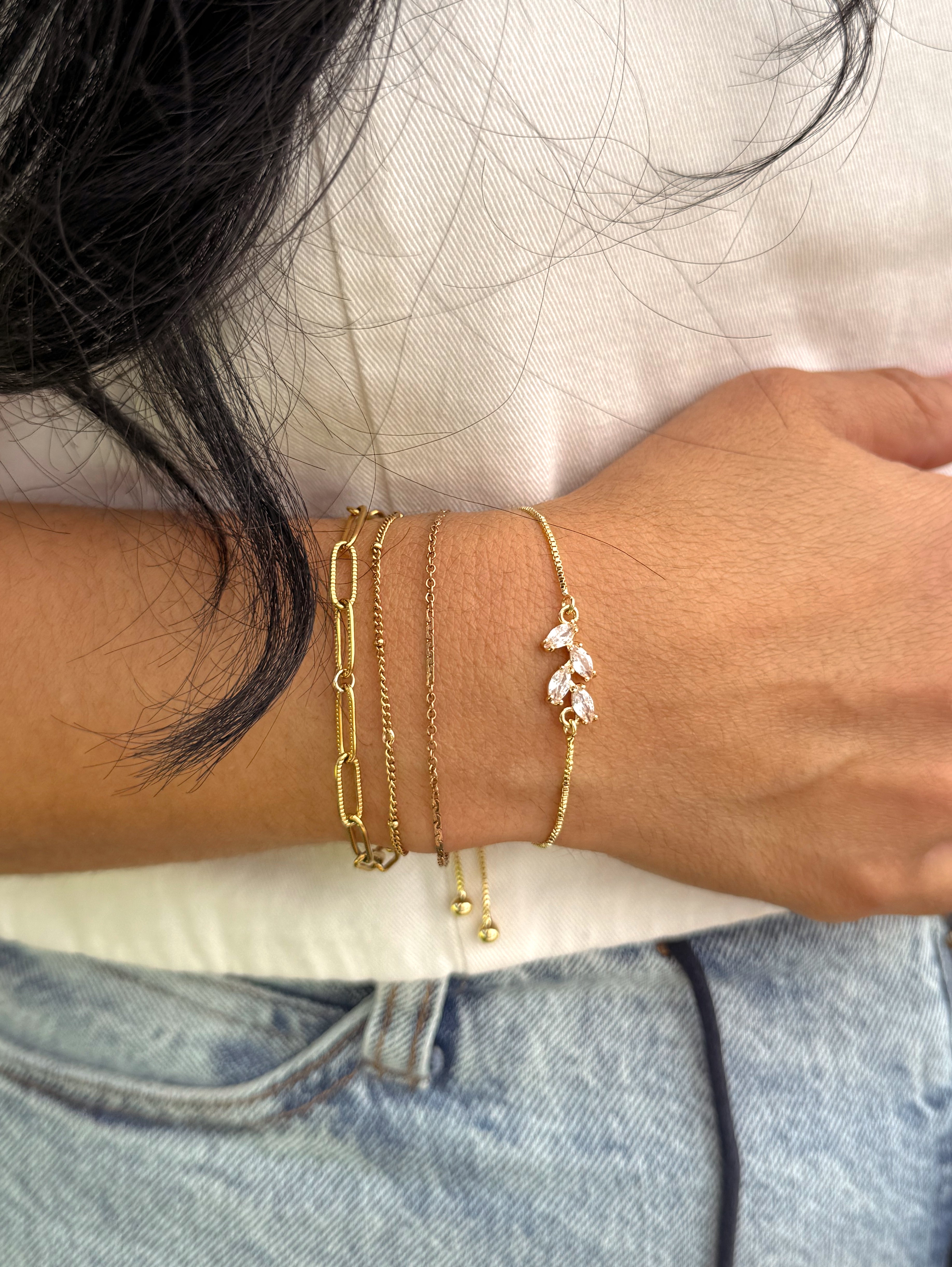 Layered gold bracelet stack featuring the Bloom Bracelet with delicate CZ vine detail, styled with dainty chain bracelets for a feminine everyday jewelry look