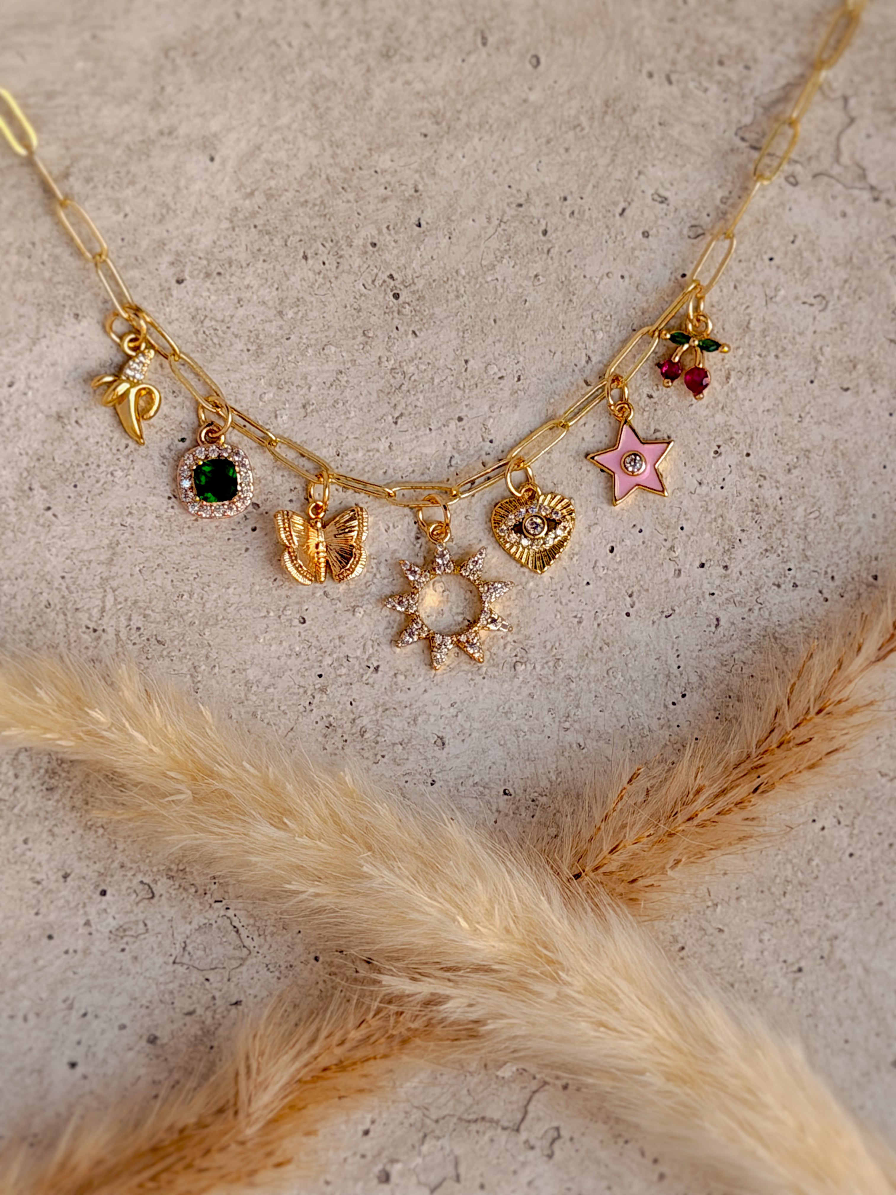 One of a Kind Cherry Charm Necklace with enamel cherry and pink star charms, cubic zirconia butterfly, heart, sun, emerald gemstone, and gold paperclip chain handcrafted by Rising Soul Jewelry.