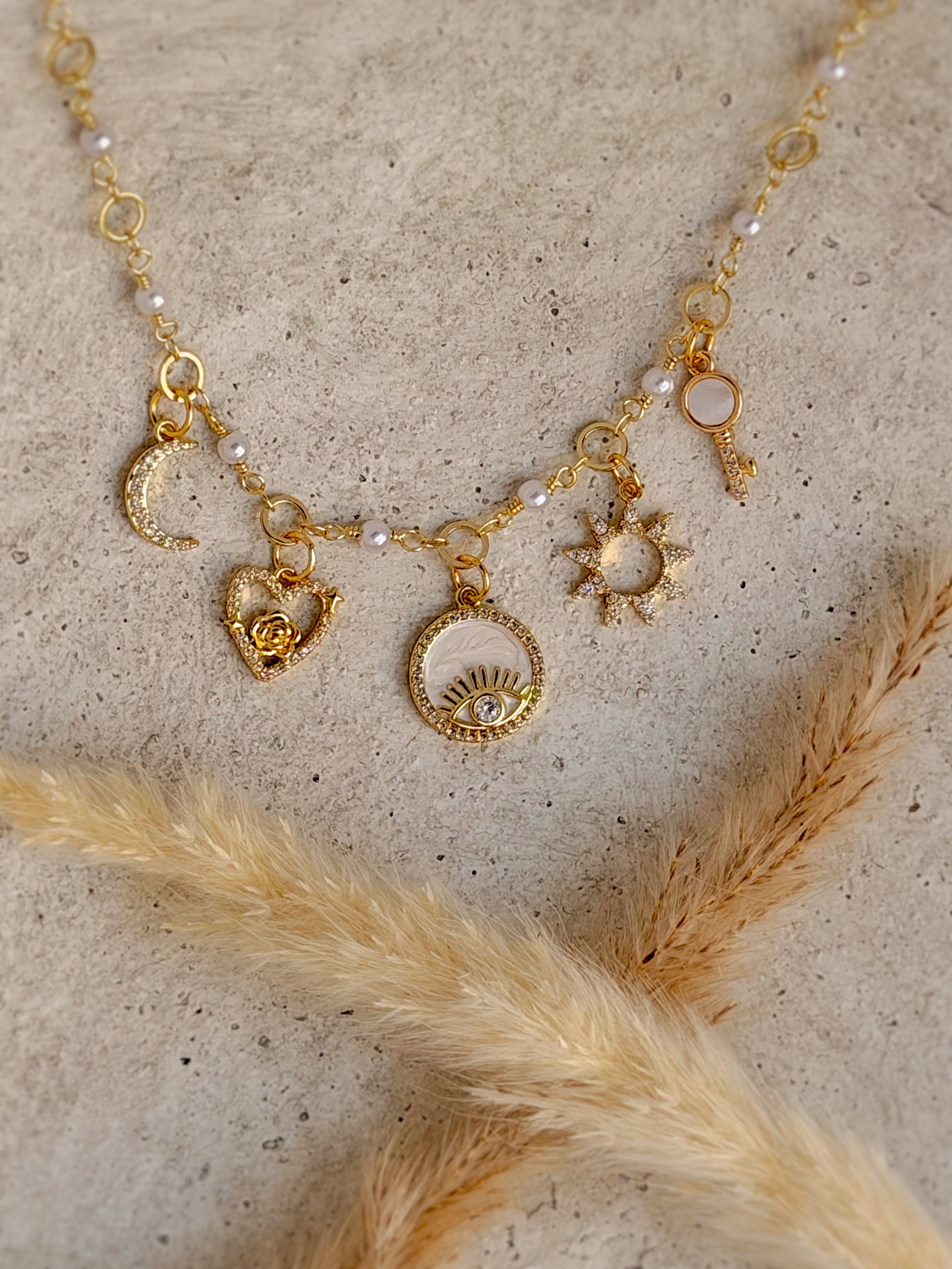 One of a Kind Evil Eye Charm Necklace with authentic freshwater pearls, genuine mother of pearl, cubic zirconia moon, sun, rose, key, and evil eye charms handcrafted by Rising Soul Jewelry.