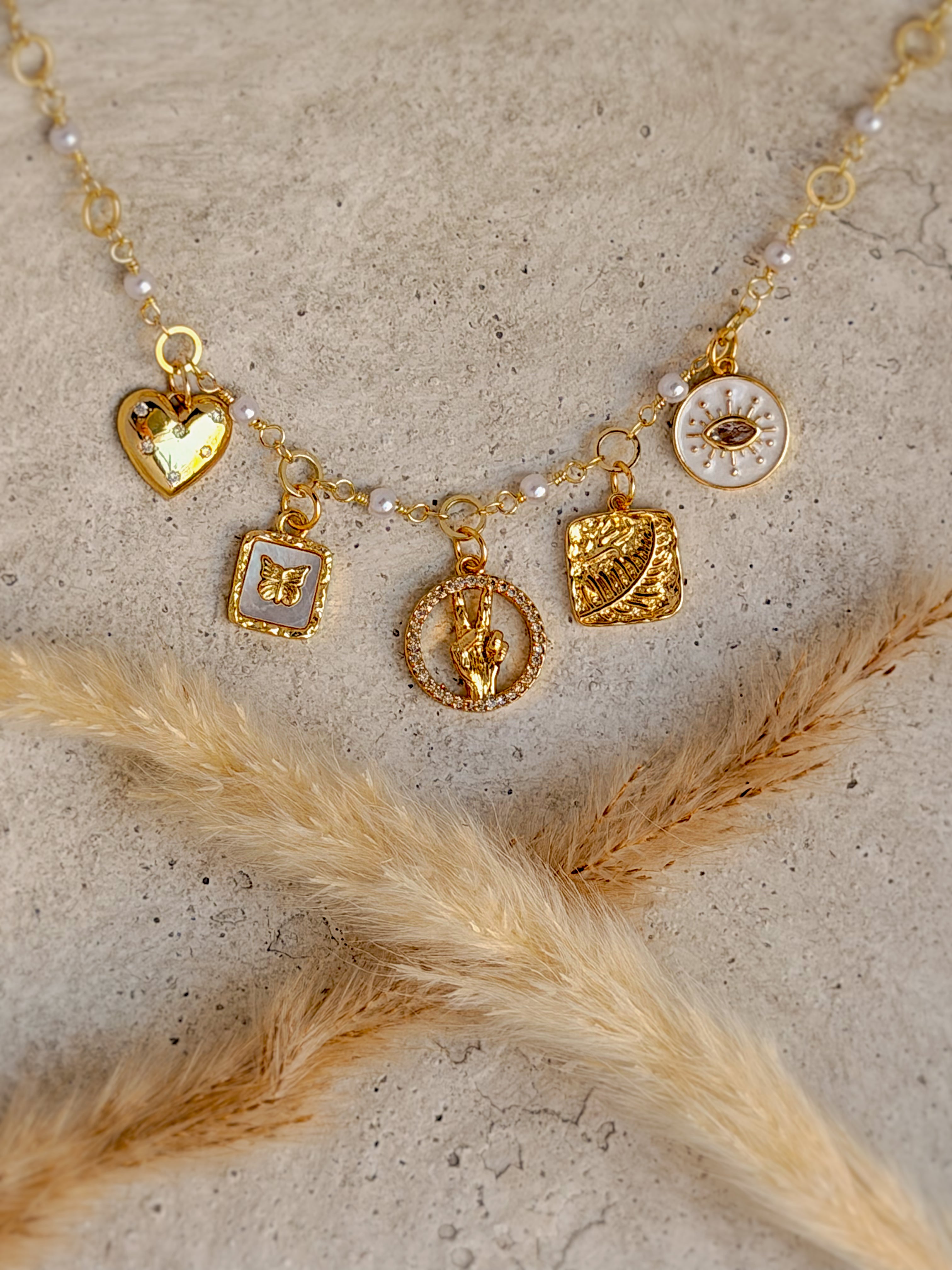 One of a Kind Evil Eye Charm Necklace with authentic freshwater pearls, genuine mother of pearl, cubic zirconia heart, butterfly, peace hand, and botanical gold charms handcrafted by Rising Soul Jewelry.