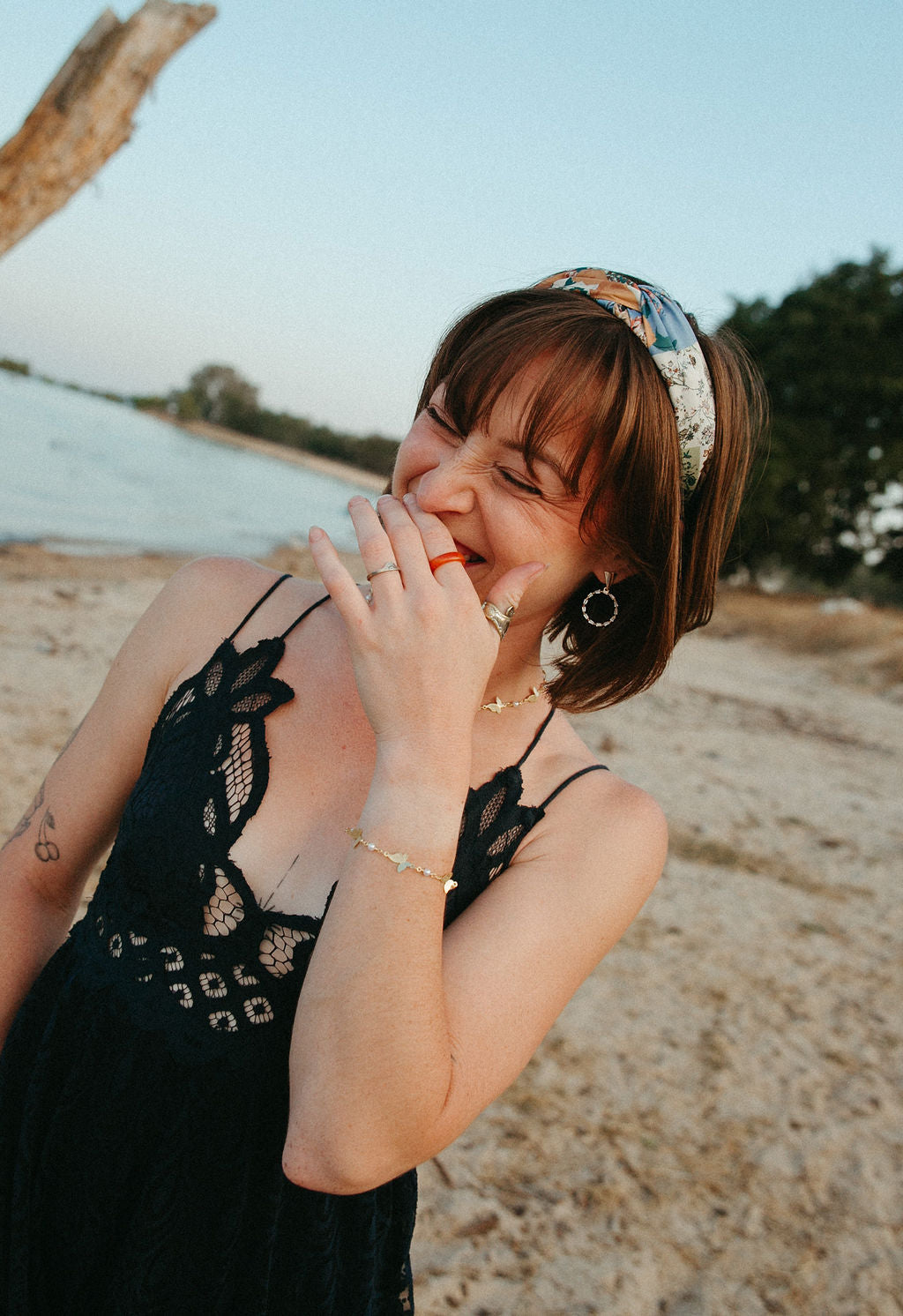 Woman smiling outdoors wearing gold circle drop earrings, radiant statement jewelry in natural beach setting