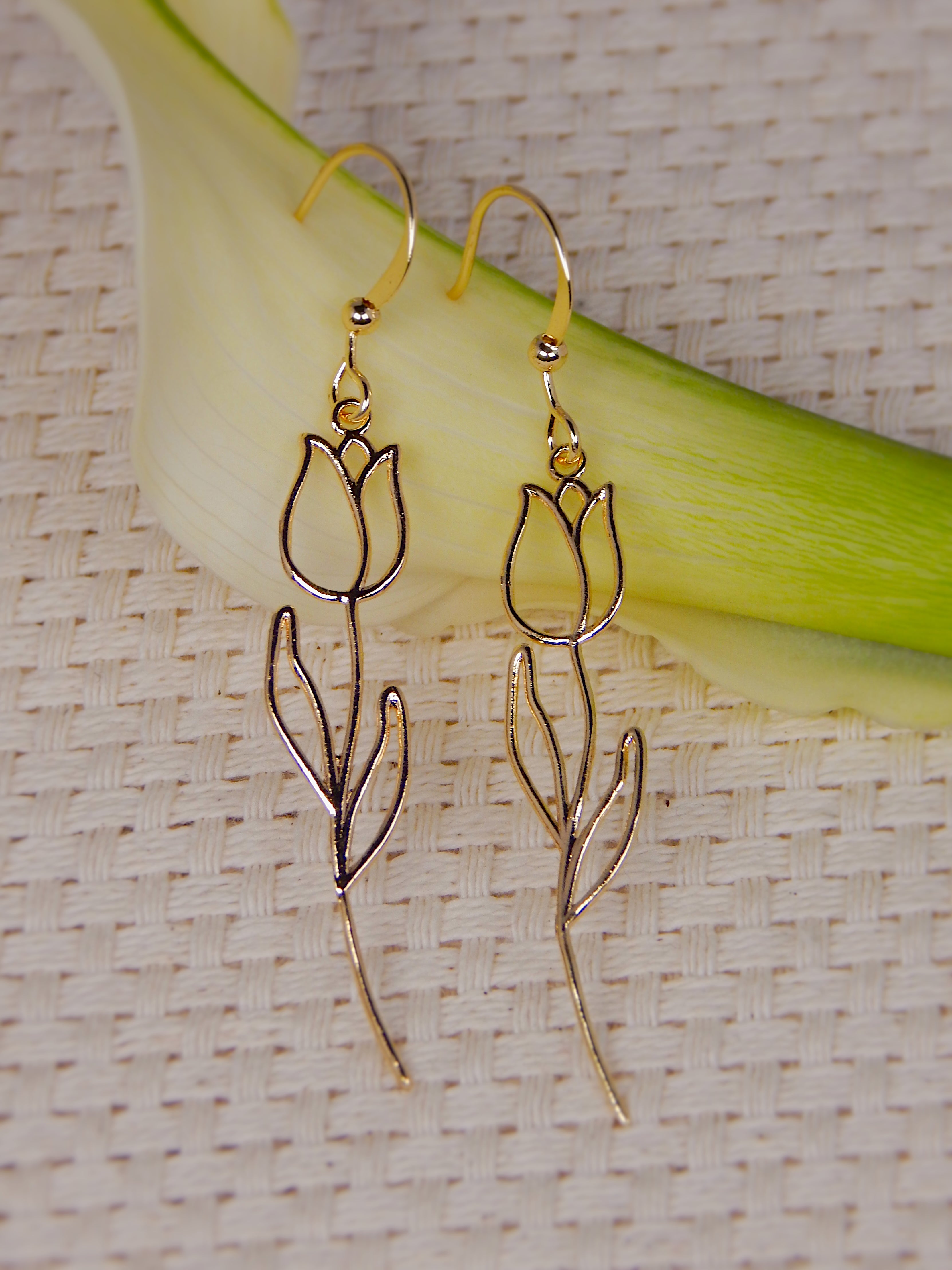Gold tulip drop earrings with minimal floral outline design displayed on textured neutral background, elegant nature-inspired jewelry
