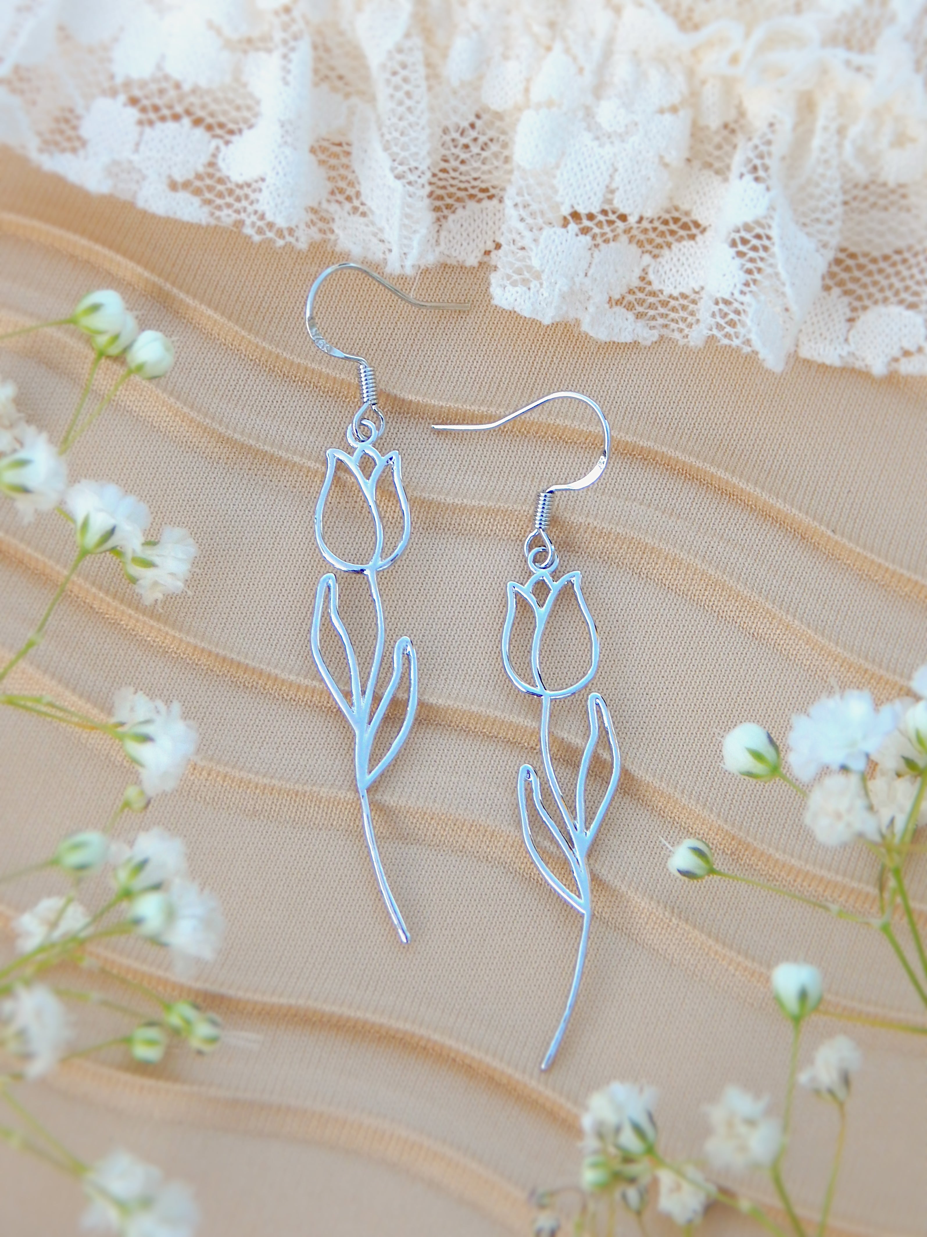 Silver tulip drop earrings with delicate floral outline and stem design displayed on soft neutral fabric with small flowers