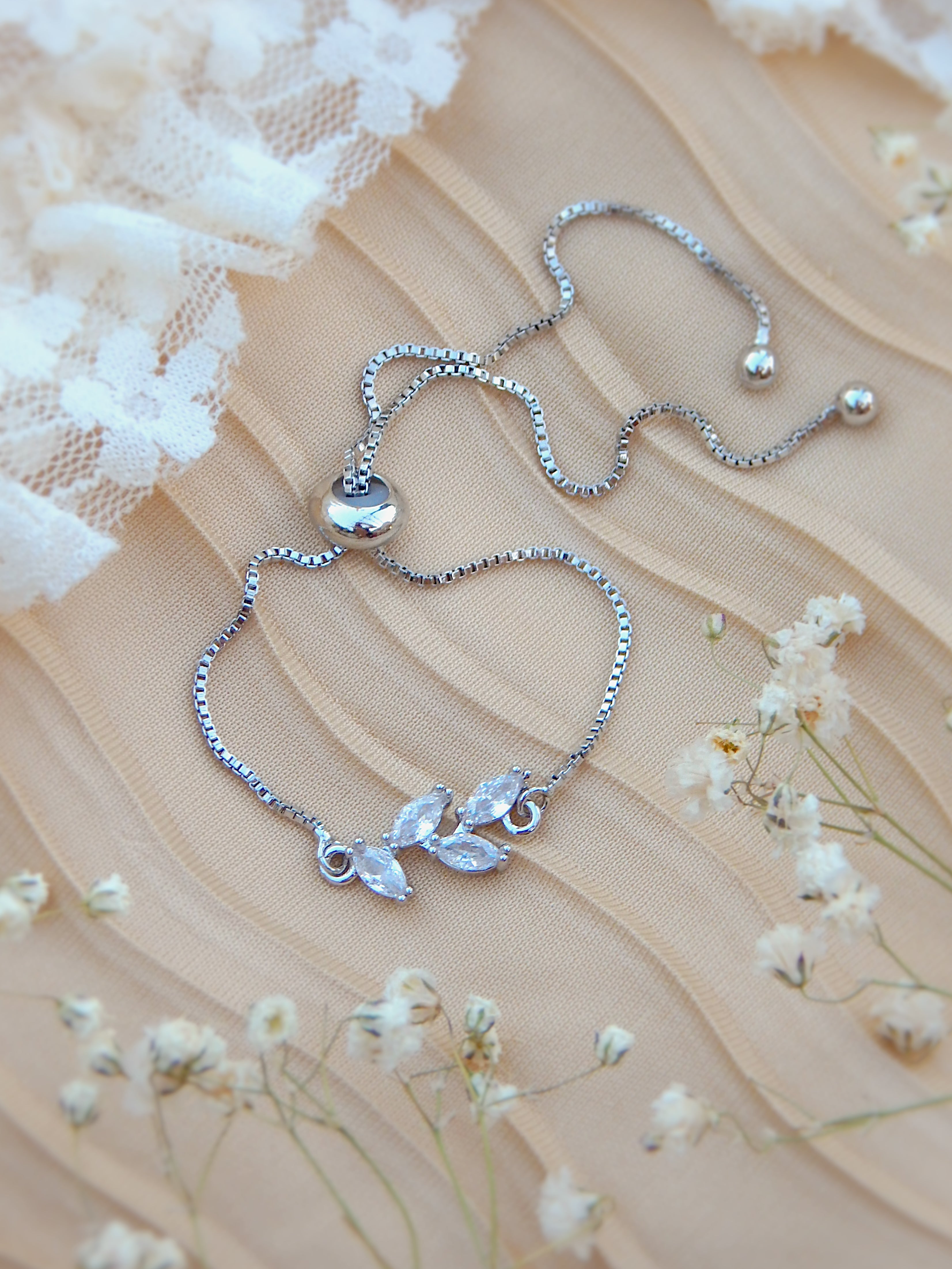 Silver floral chain bracelet with adjustable bead clasp on neutral surface with soft florals