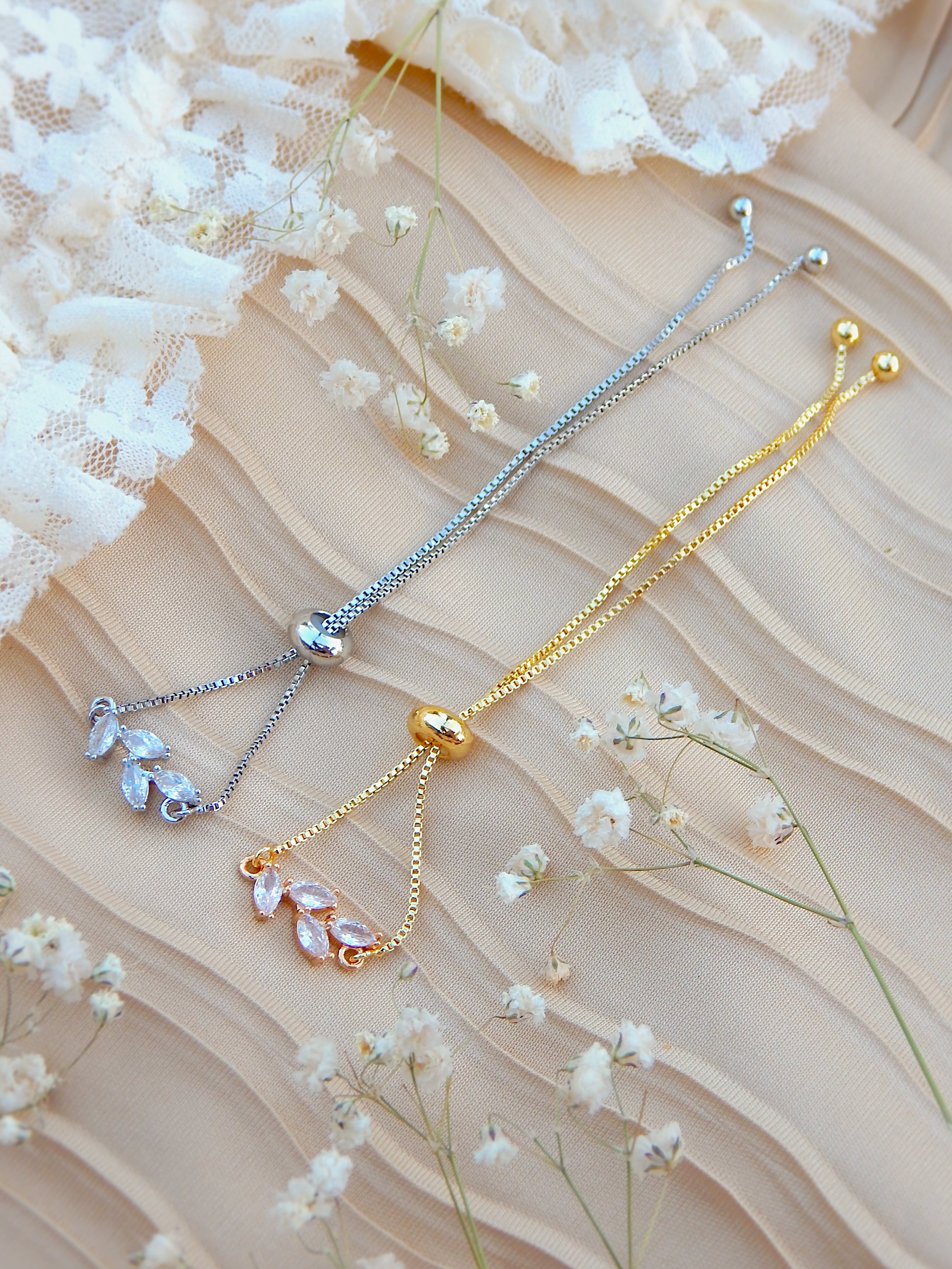 Gold and silver bloom bracelets with floral charms styled with white flowers on neutral background