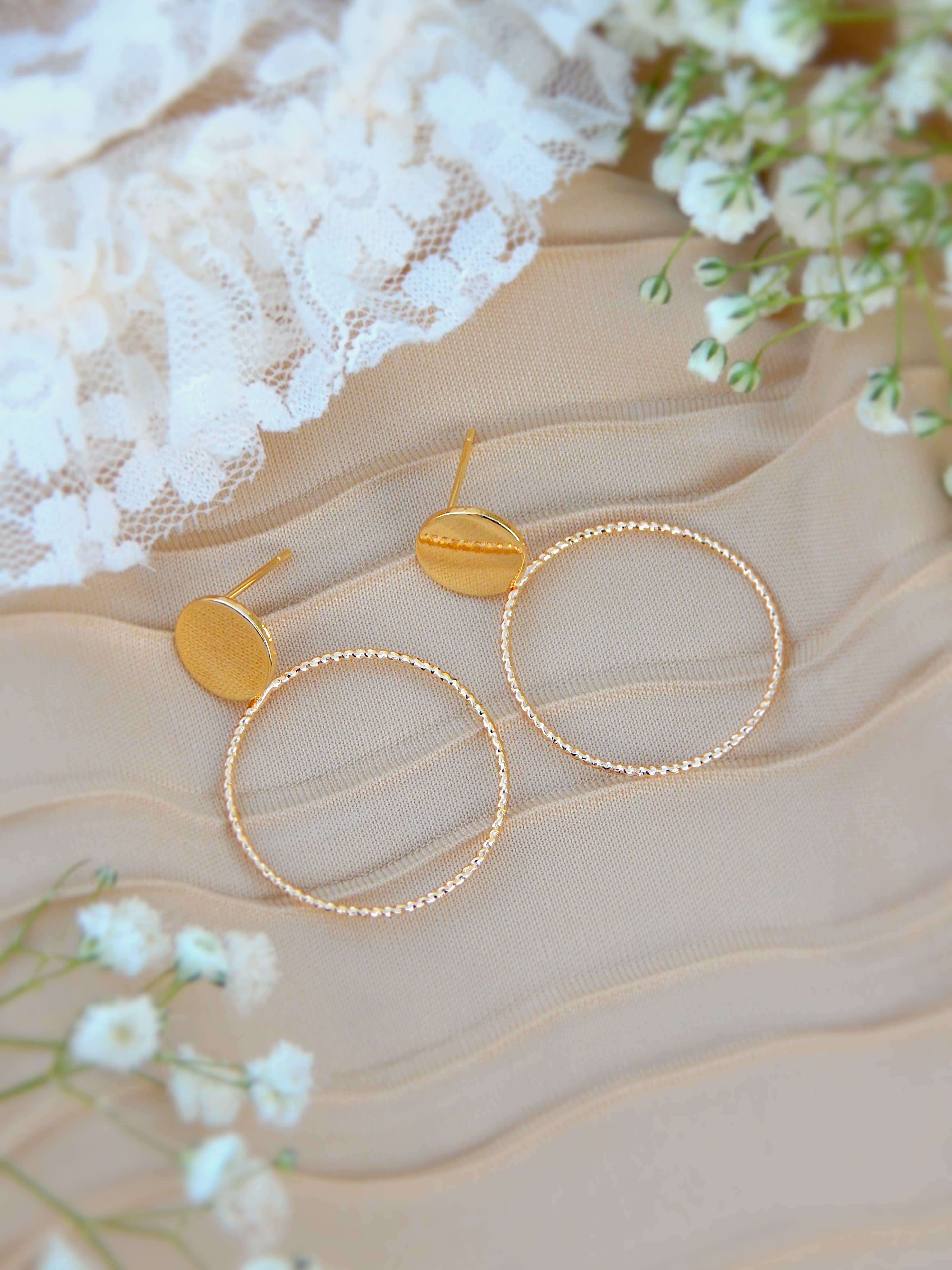 Gold hoop earrings on a textured beige surface with white lace and flowers.