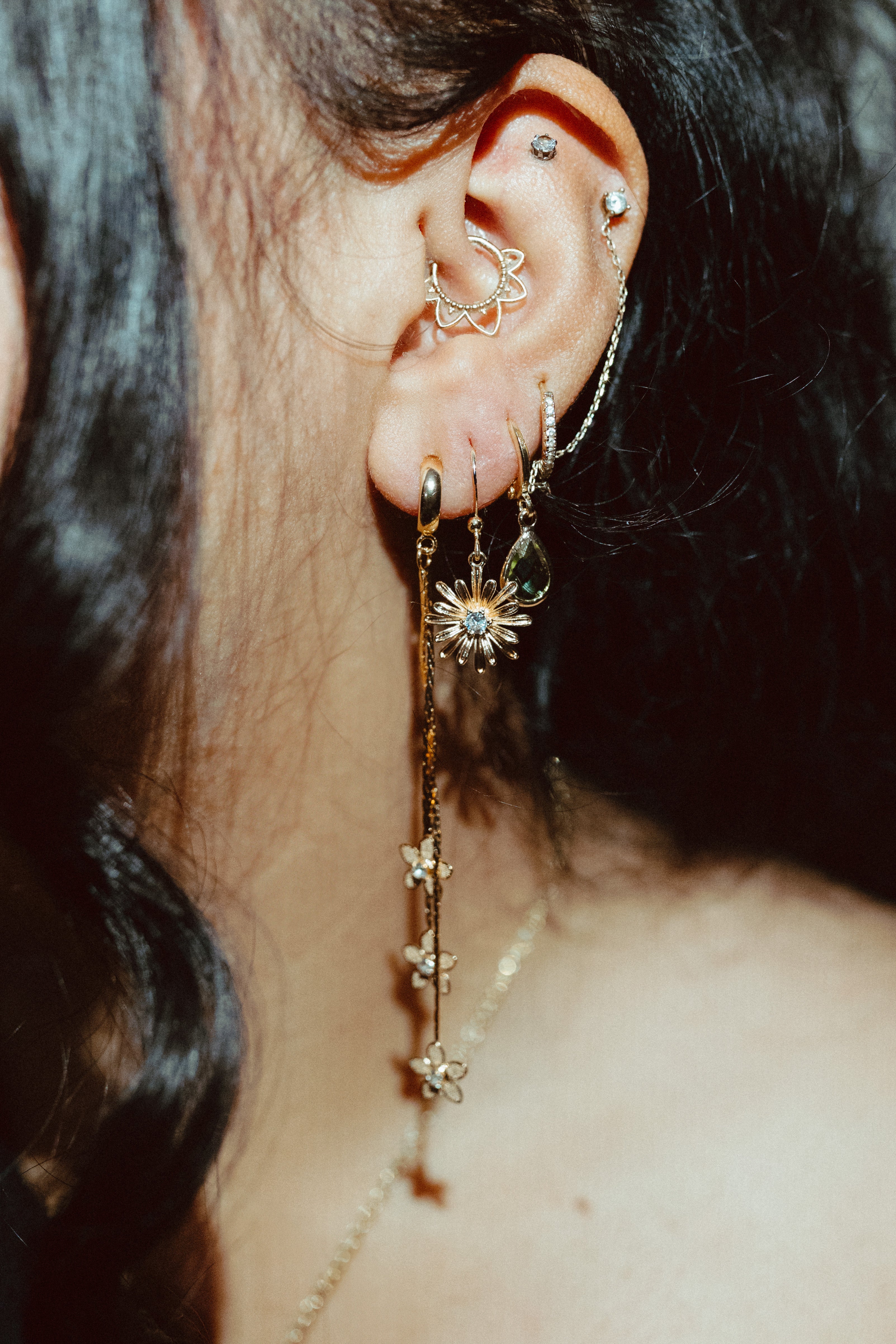Gold huggie earrings styled in ear stack with dangling details, layered jewelry look