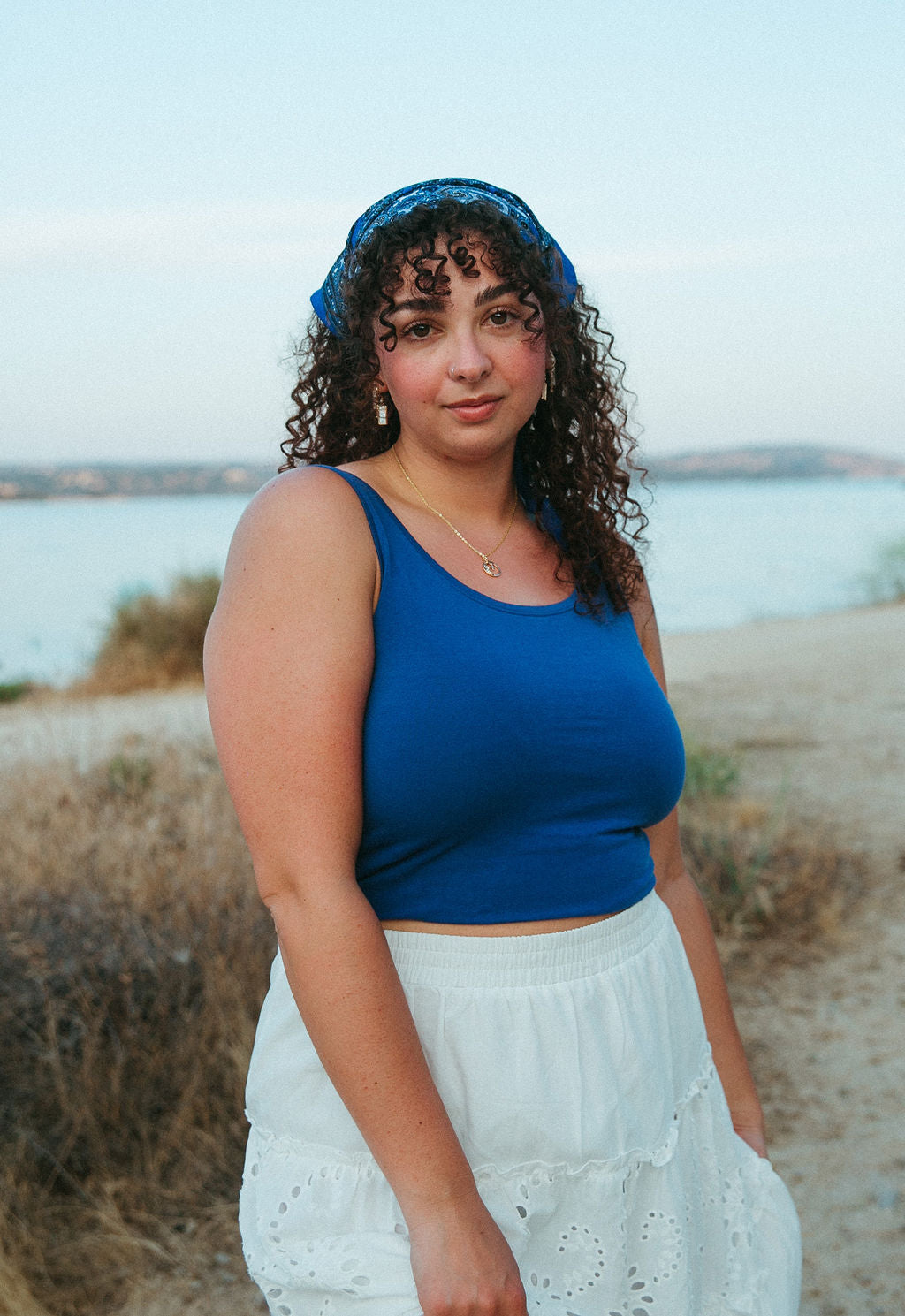 Woman wearing gold rectangle mother of pearl earrings styled with casual outfit outdoors near water