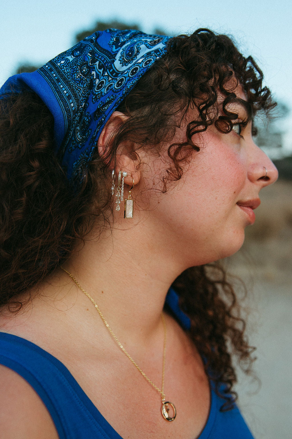 Side profile of woman wearing rectangular mother of pearl earrings in gold, styled in natural outdoor lighting