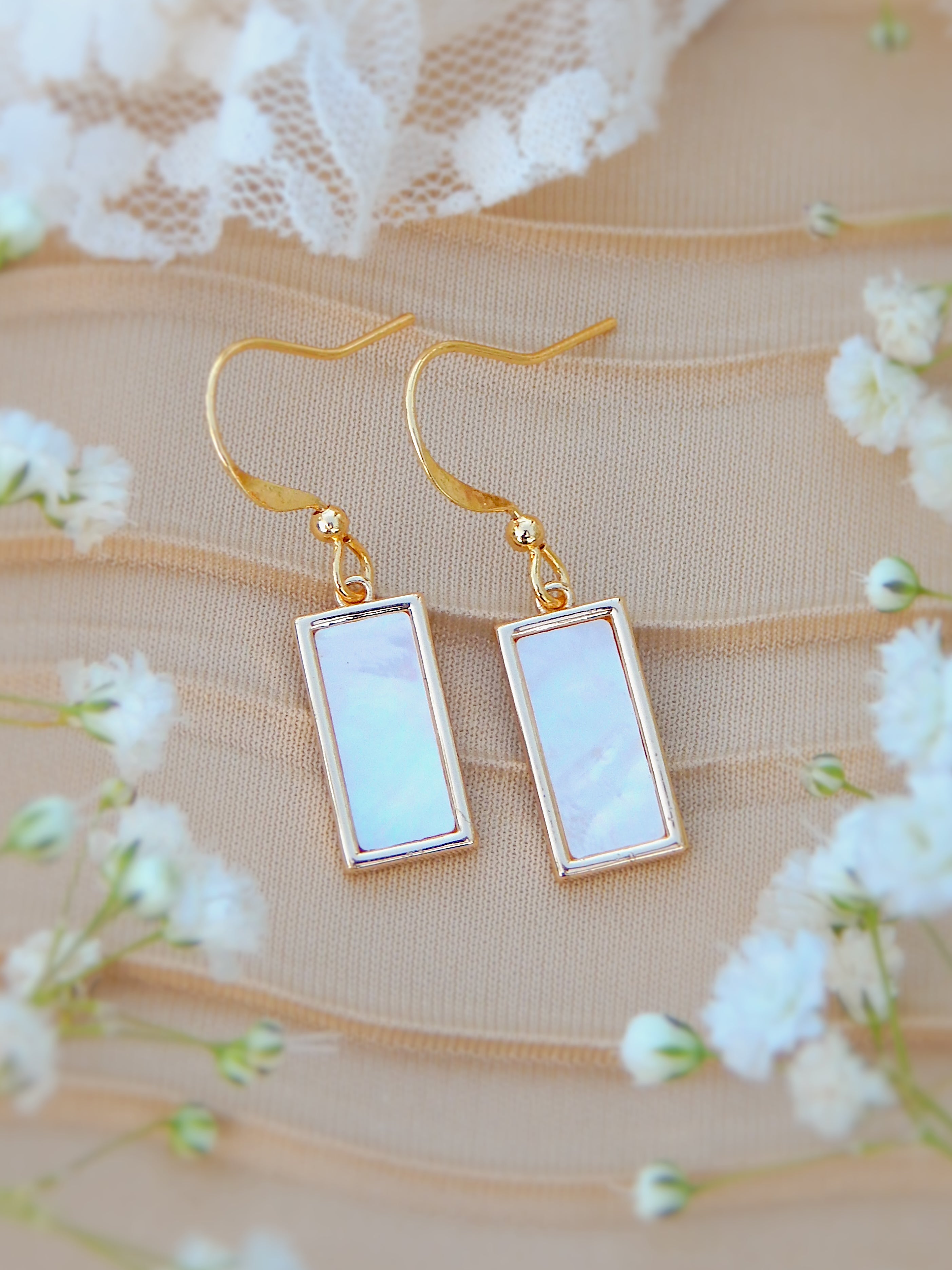 Gold rectangle earrings with authentic mother of pearl displayed on soft fabric with floral details, minimal elegant jewelry design