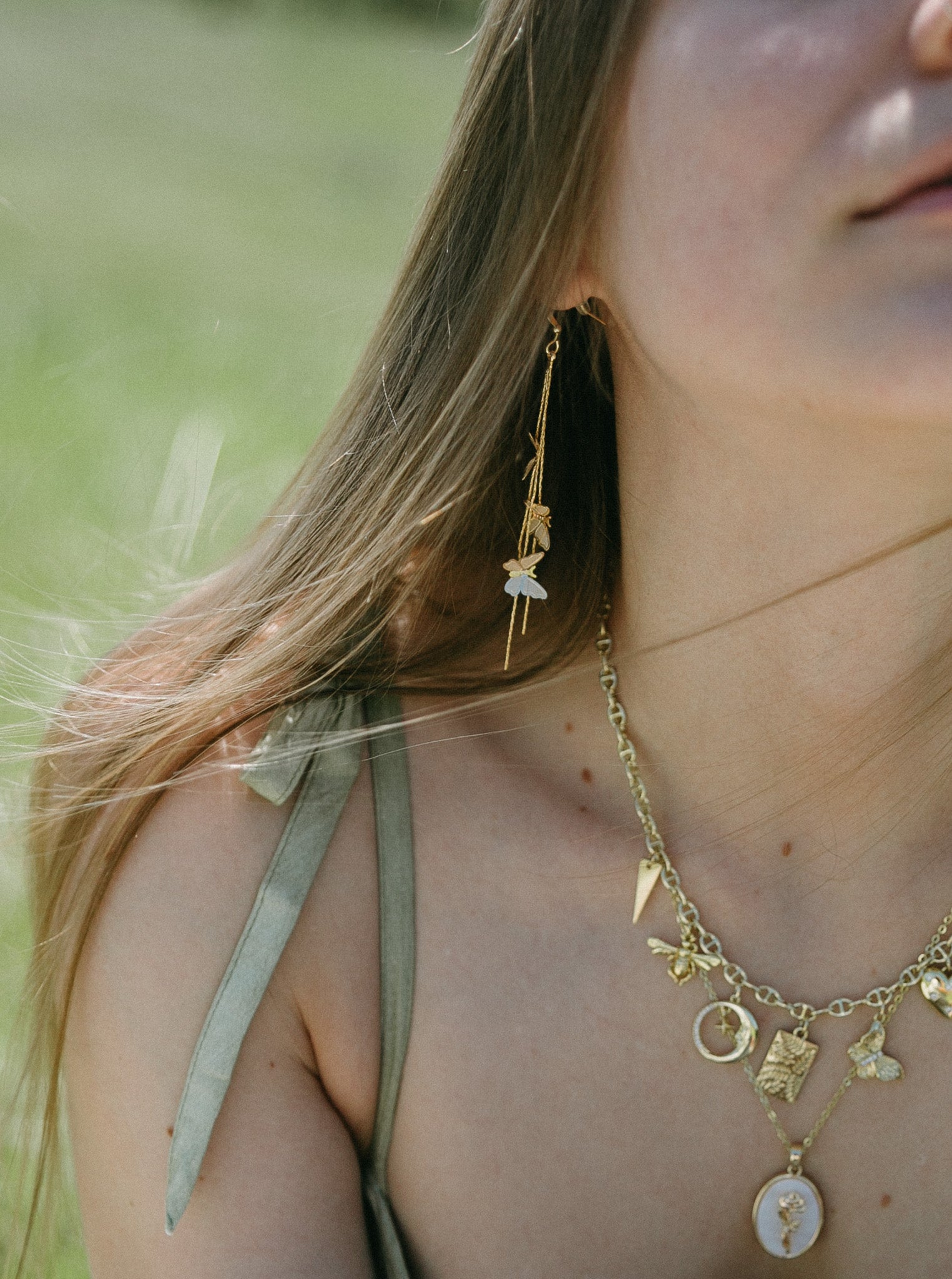 Close-up of gold butterfly drop earrings with layered chains styled with gold necklace