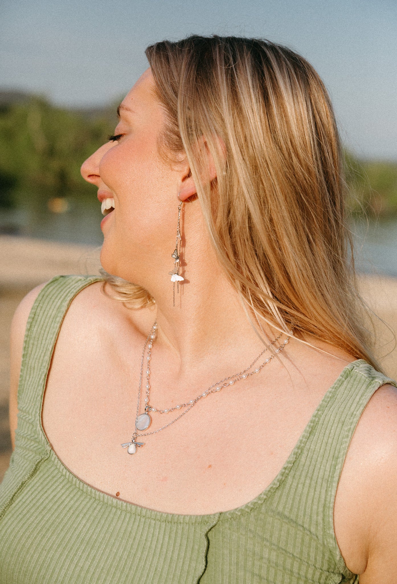 Blonde woman wearing silver butterfly drop earrings with cascading chains near beach