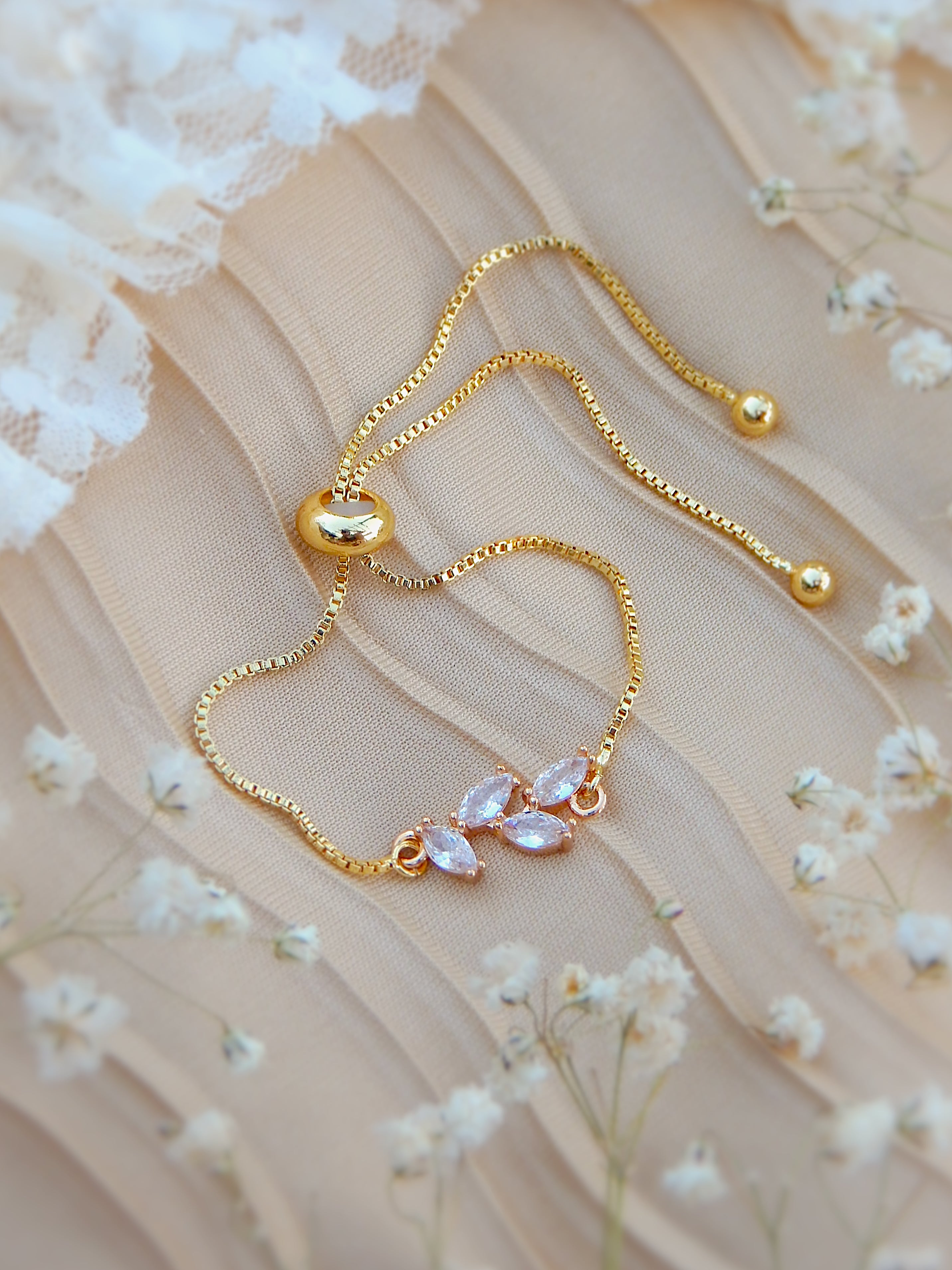 Gold bloom bracelet with delicate floral charm details on neutral surface with soft white flowers
