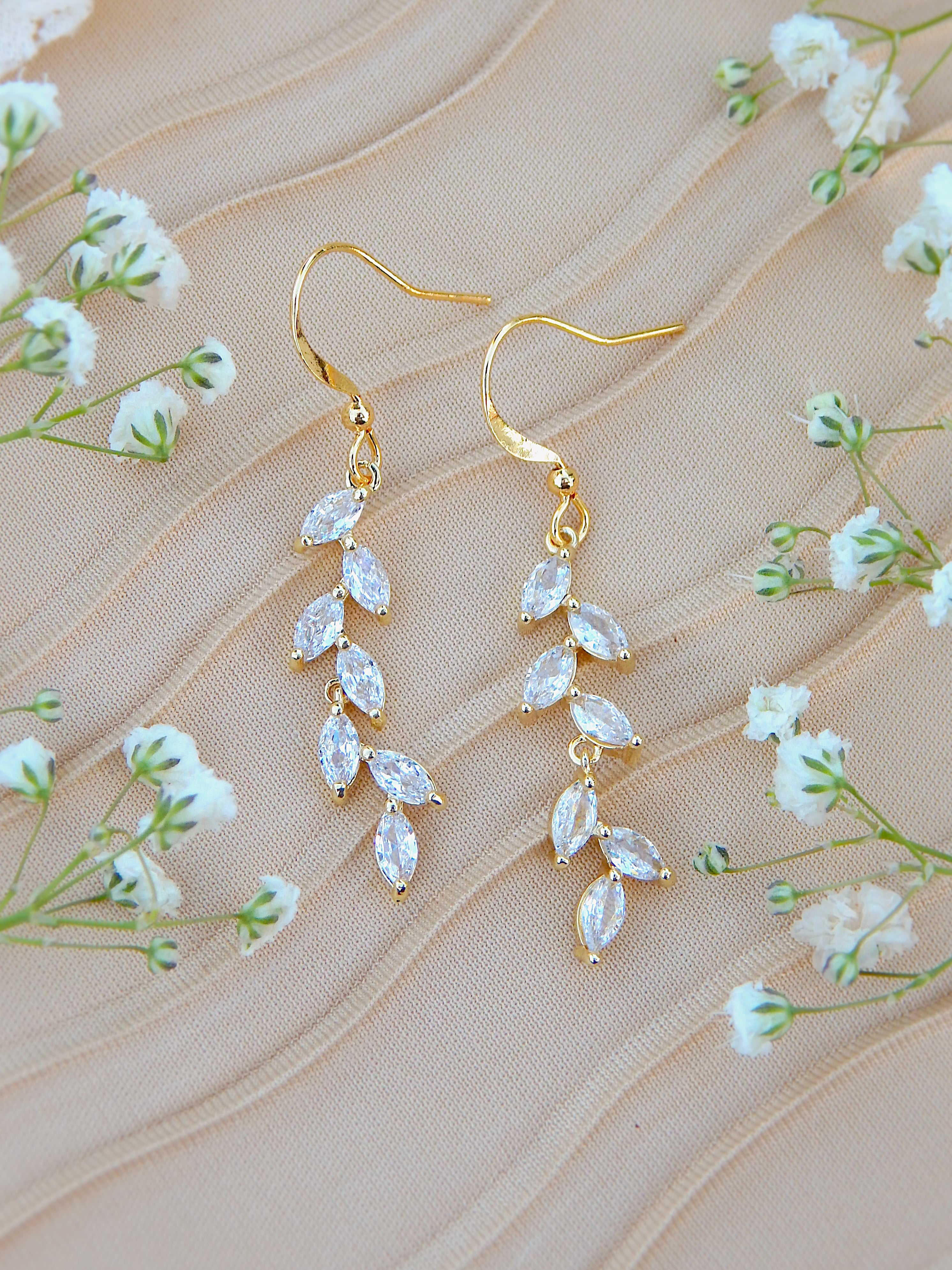 Gold cubic zirconia vine earrings with leaf design on neutral background