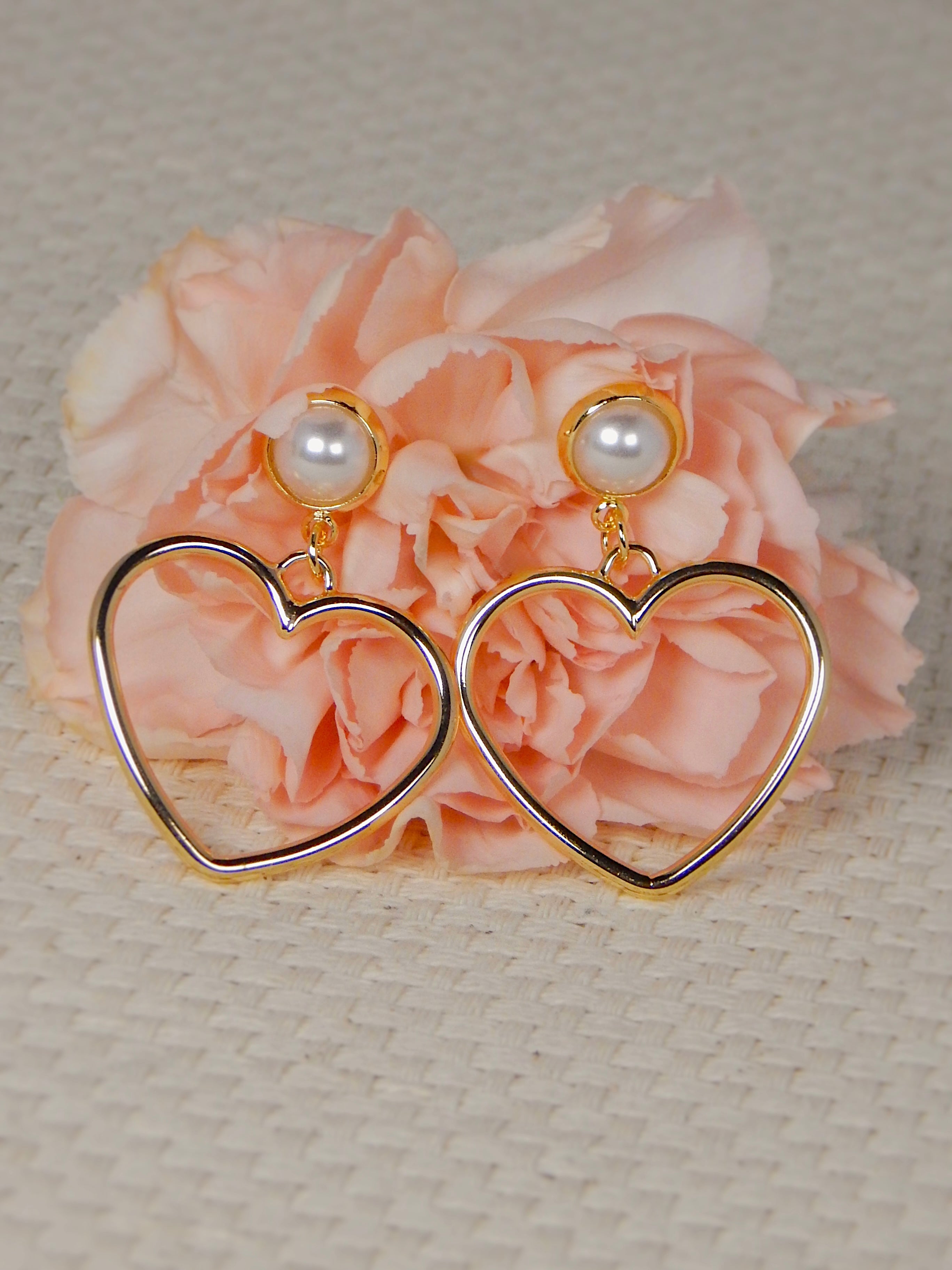 Gold heart drop earrings with pearl stud on neutral background