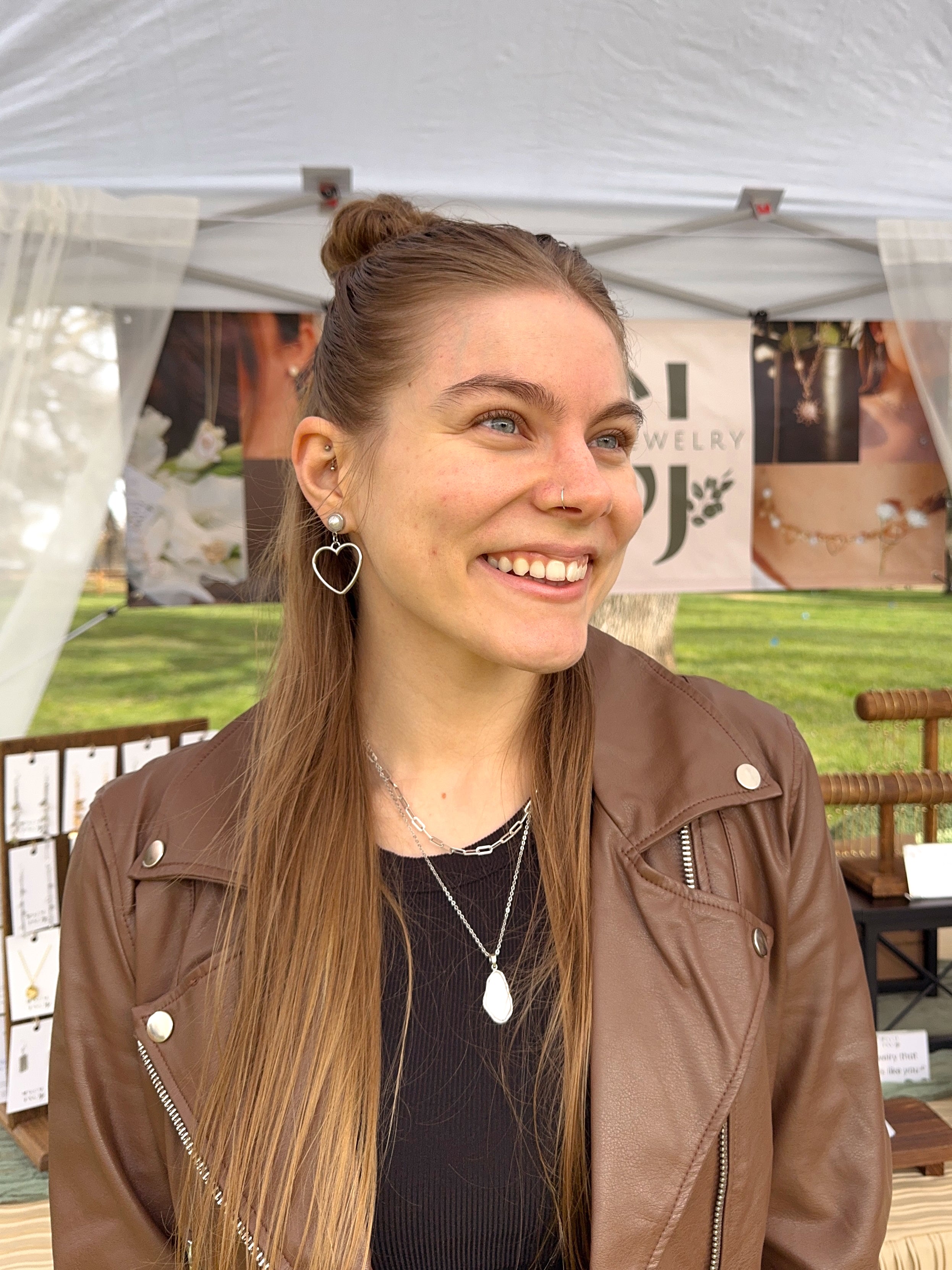 Woman wearing gold heart drop earrings with pearl stud at outdoor market booth