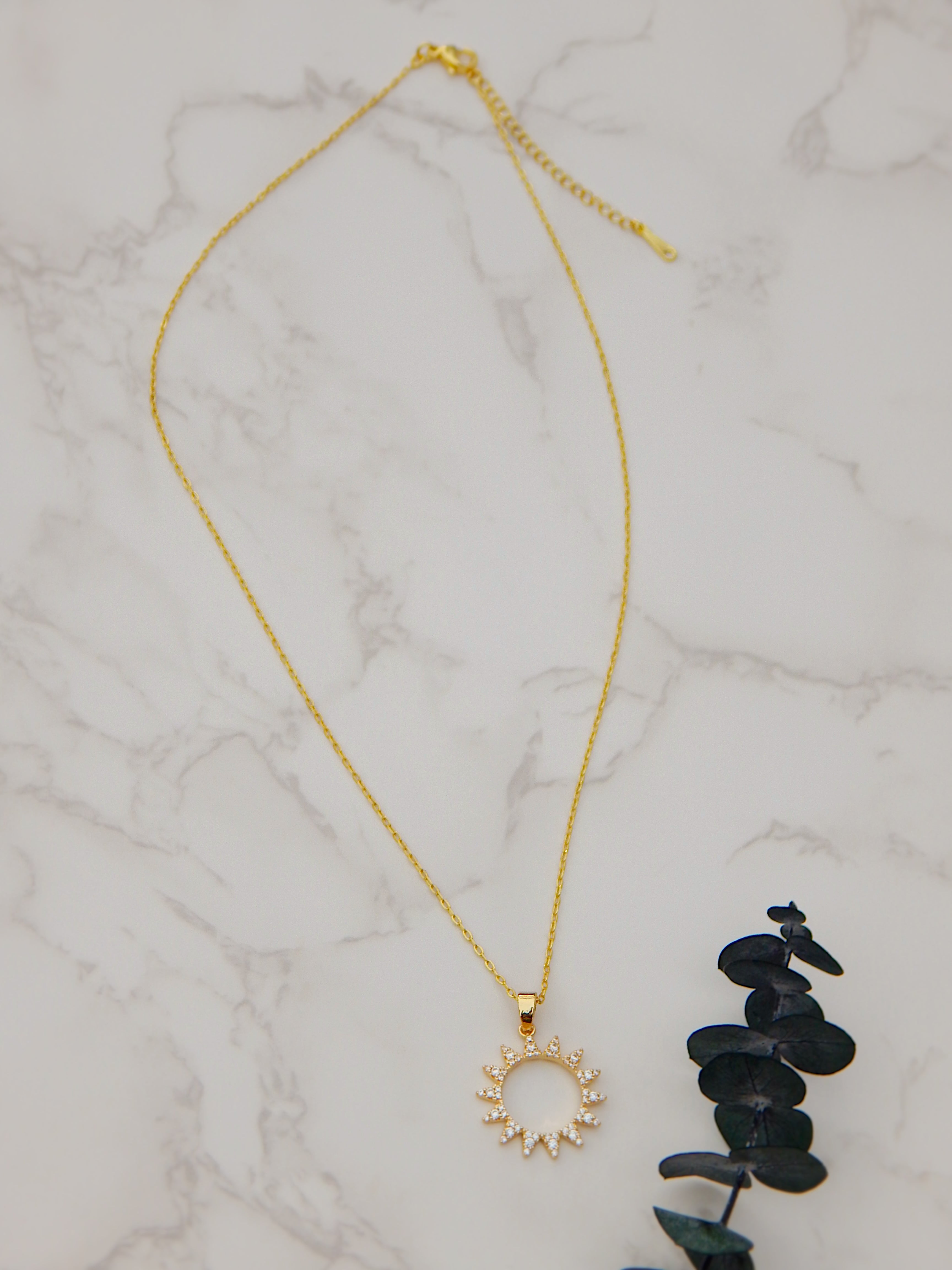Full gold necklace with sunburst cubic zirconia pendant on marble background