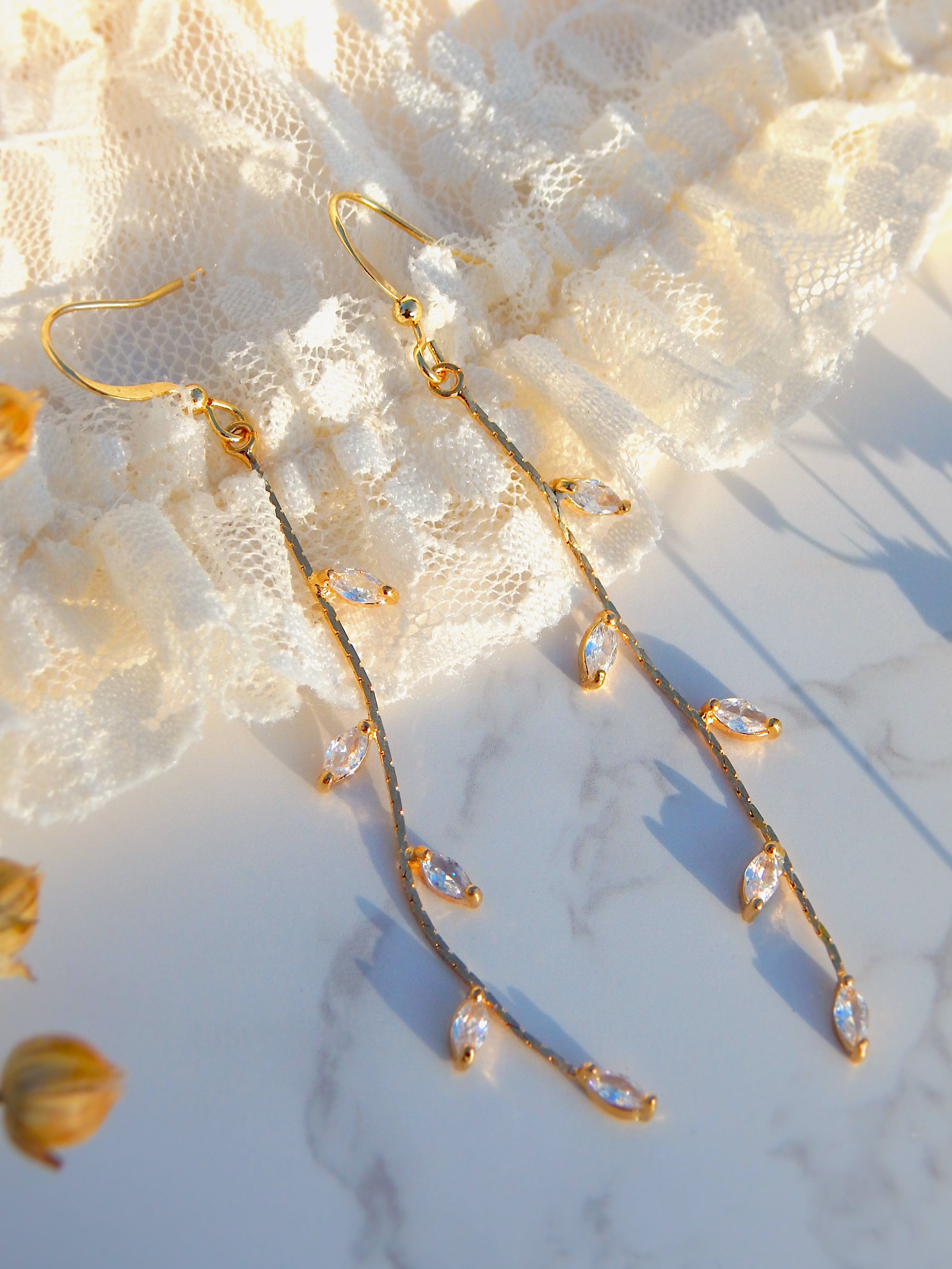 Gold vine drop earrings with marquise leaf details displayed on soft lace background, elegant nature-inspired jewelry