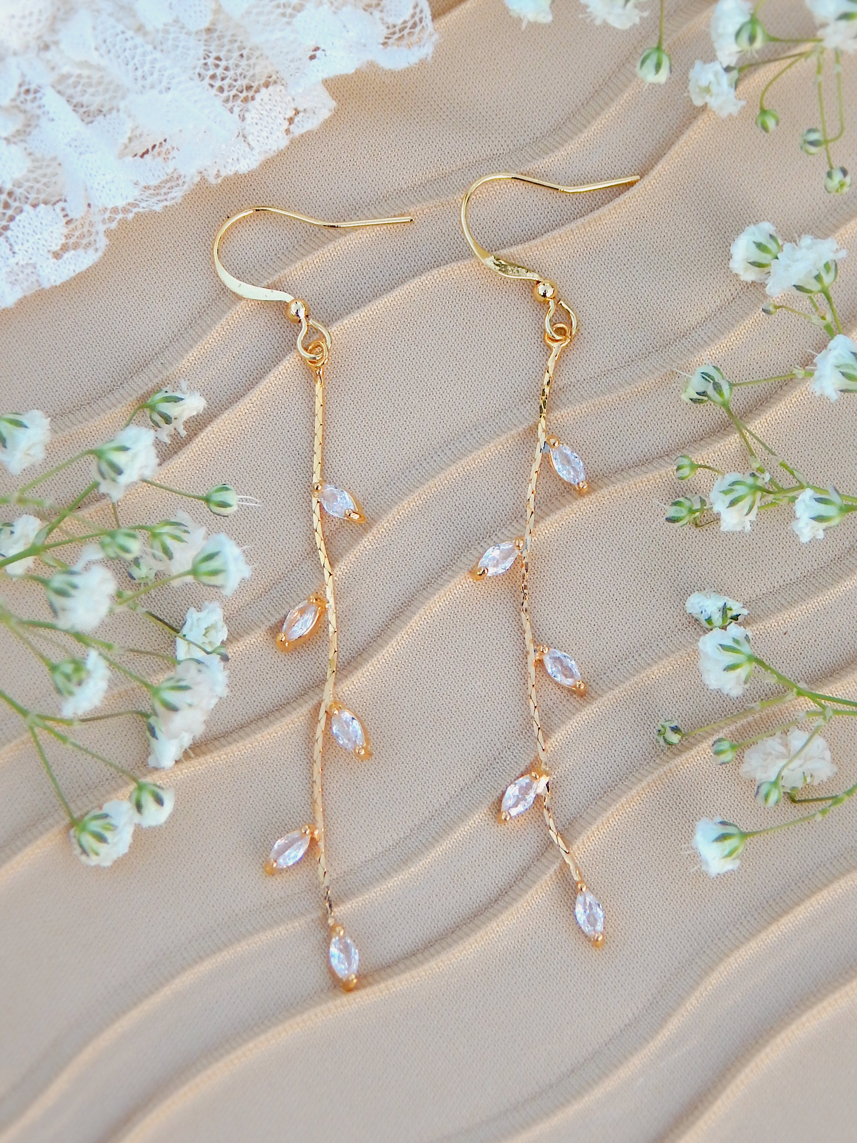 Gold vine drop earrings with leaf design displayed on soft fabric with small flowers, nature-inspired jewelry styling