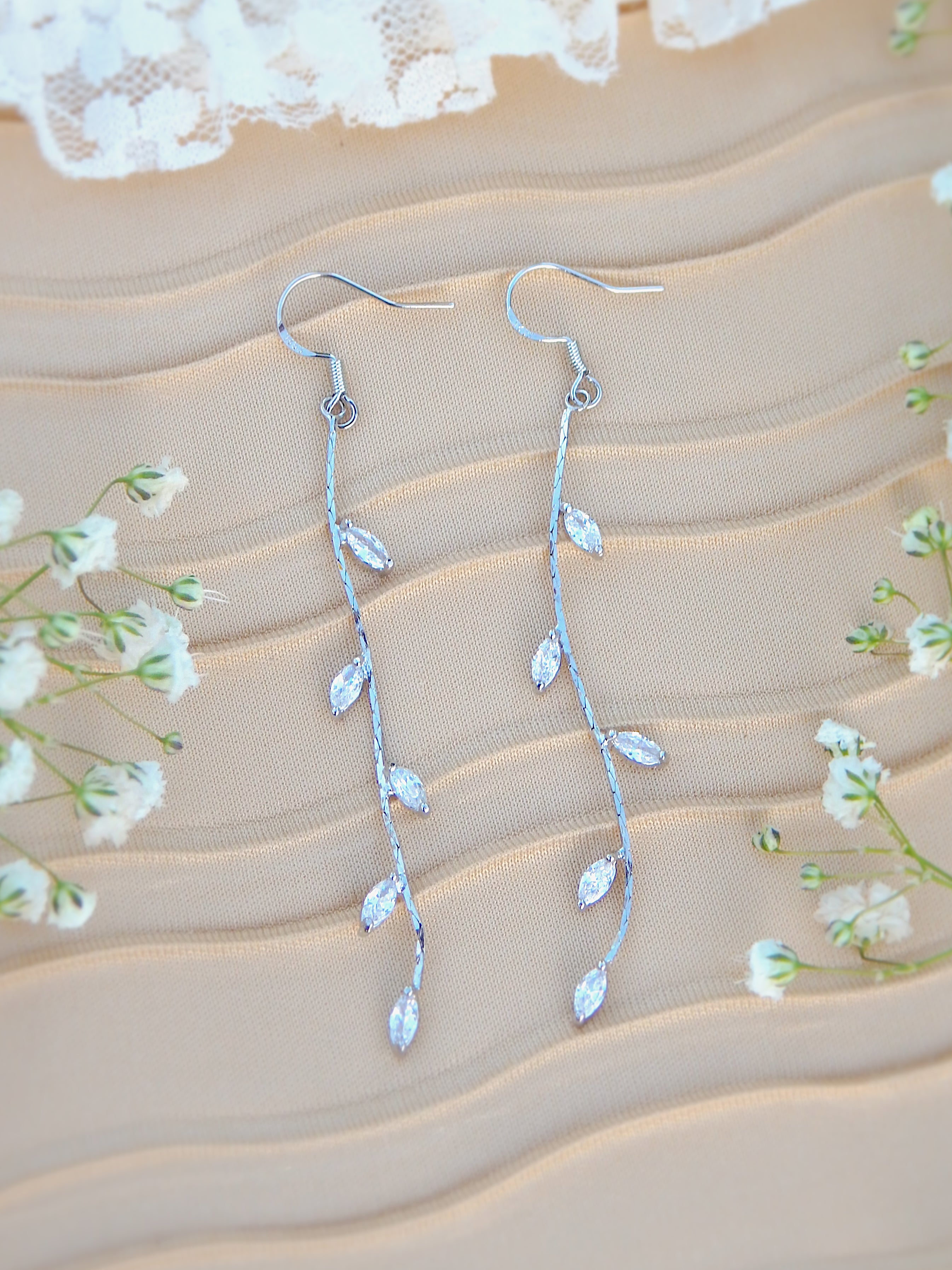 Silver vine drop earrings with marquise leaf details on neutral background with floral accents