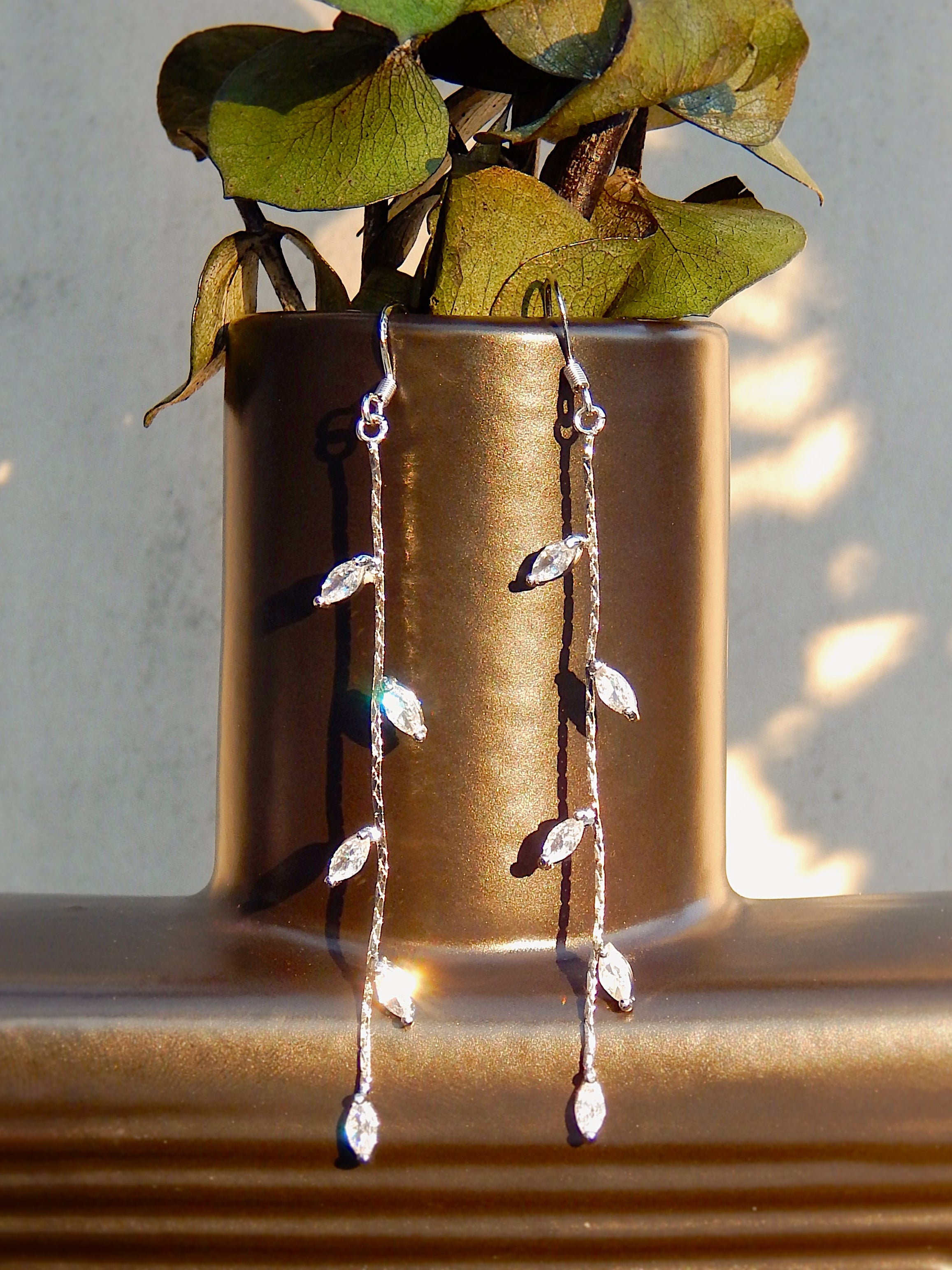 Silver vine drop earrings with leaf details hanging on vase, featuring long delicate dangle design with cubic zirconia accents
