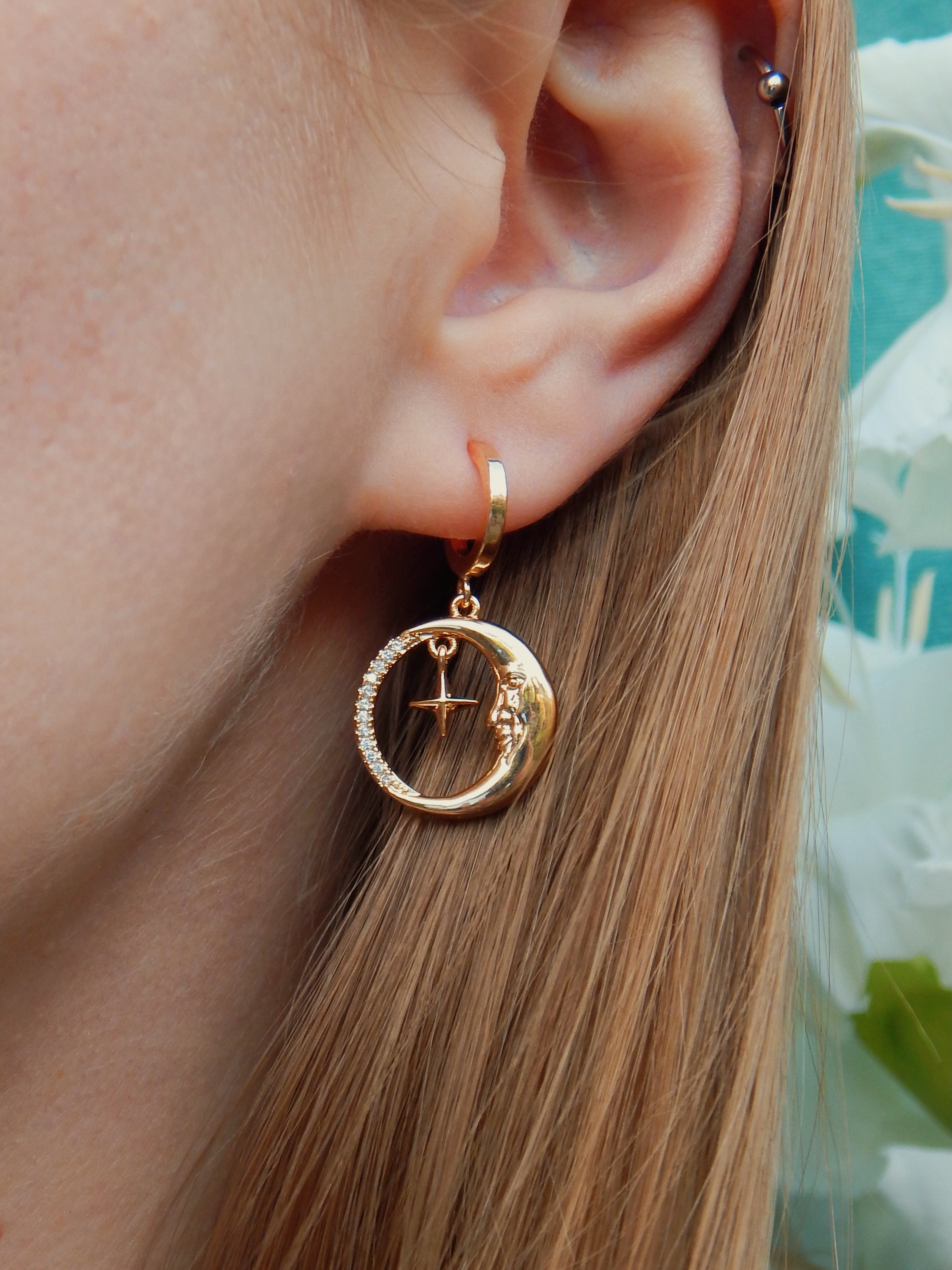 Close-up of gold moon and star huggie earrings worn on ear