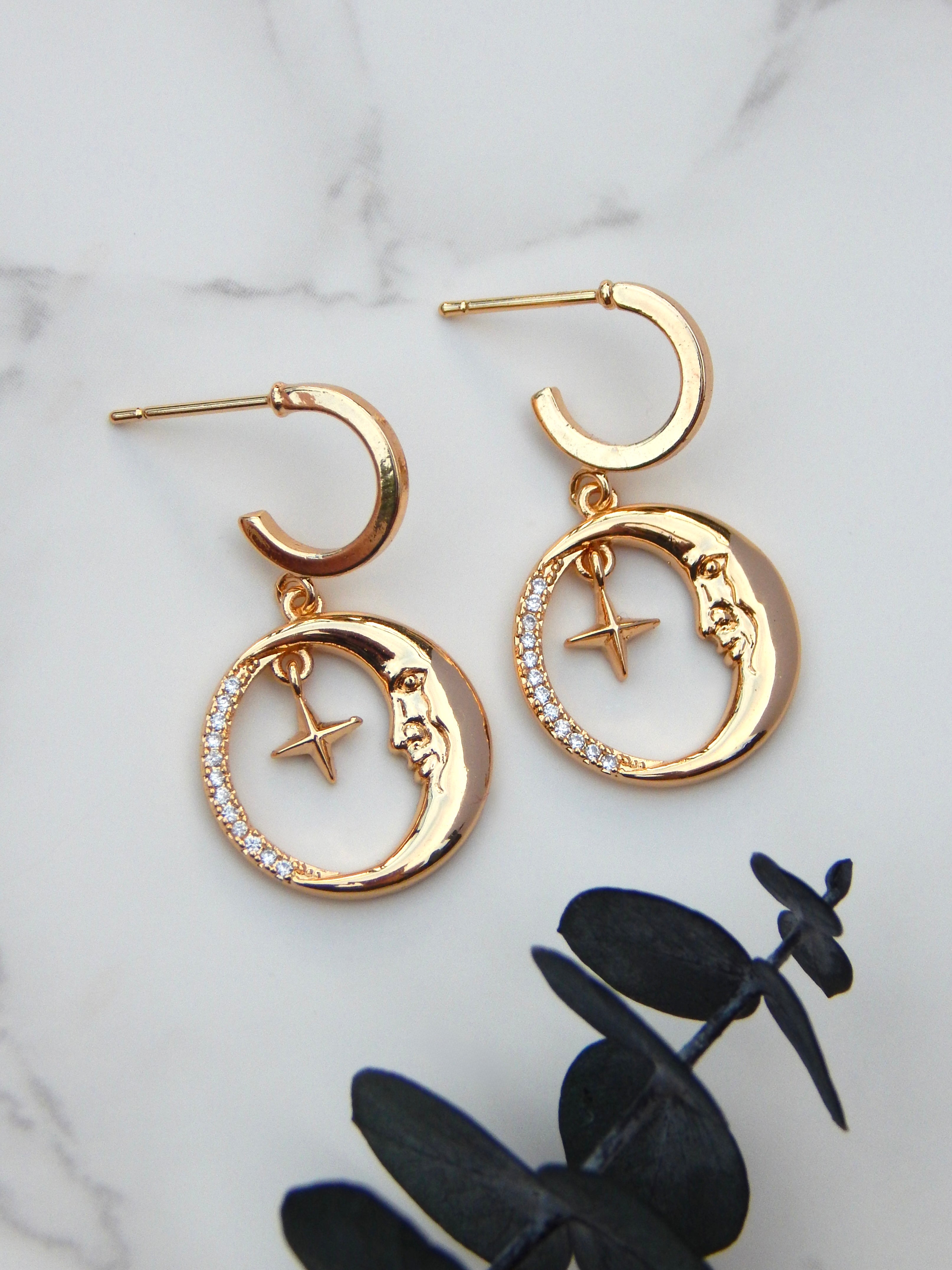 Gold moon and star huggie earrings on marble background