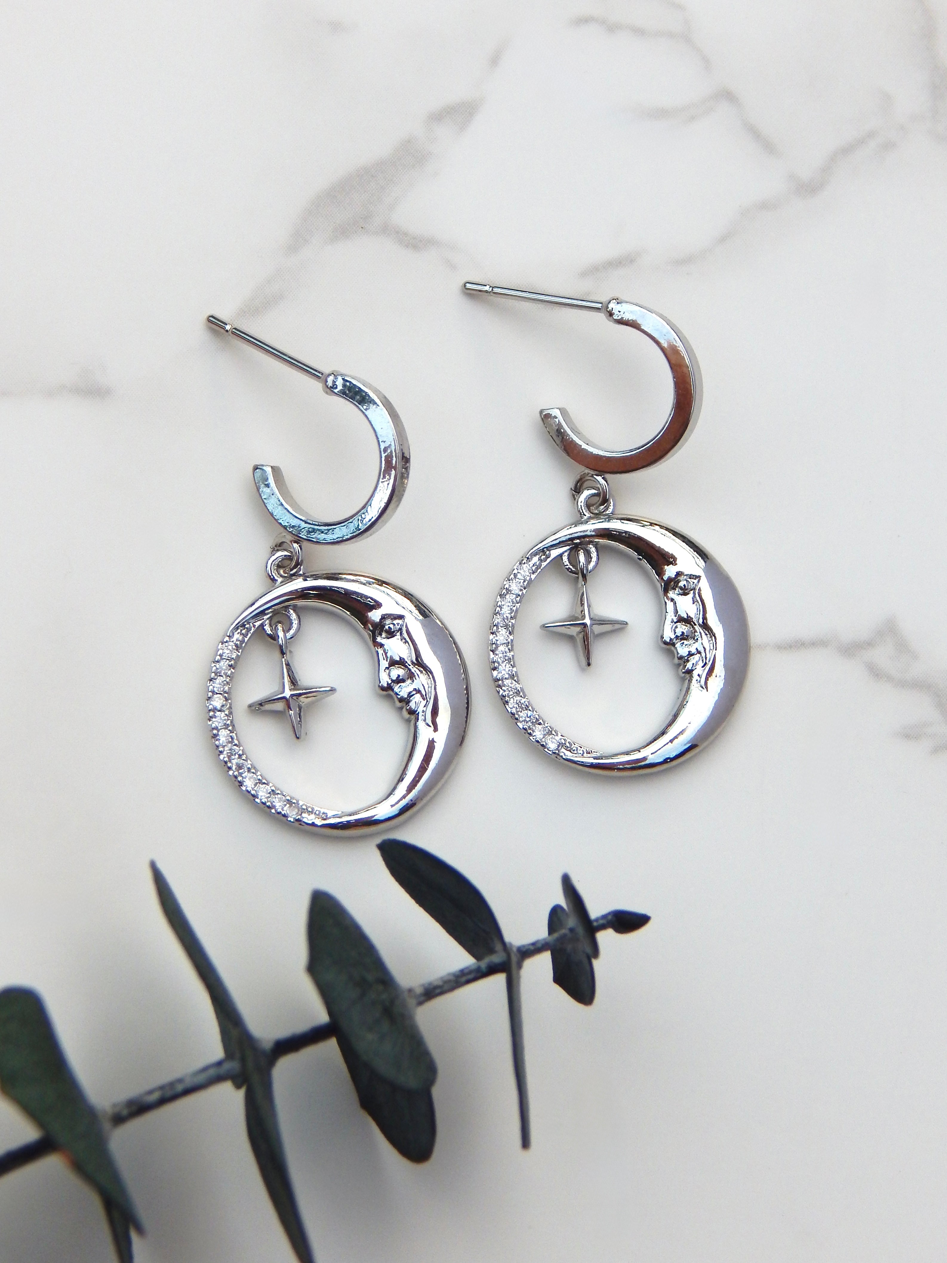 Silver moon and star huggie earrings on marble background