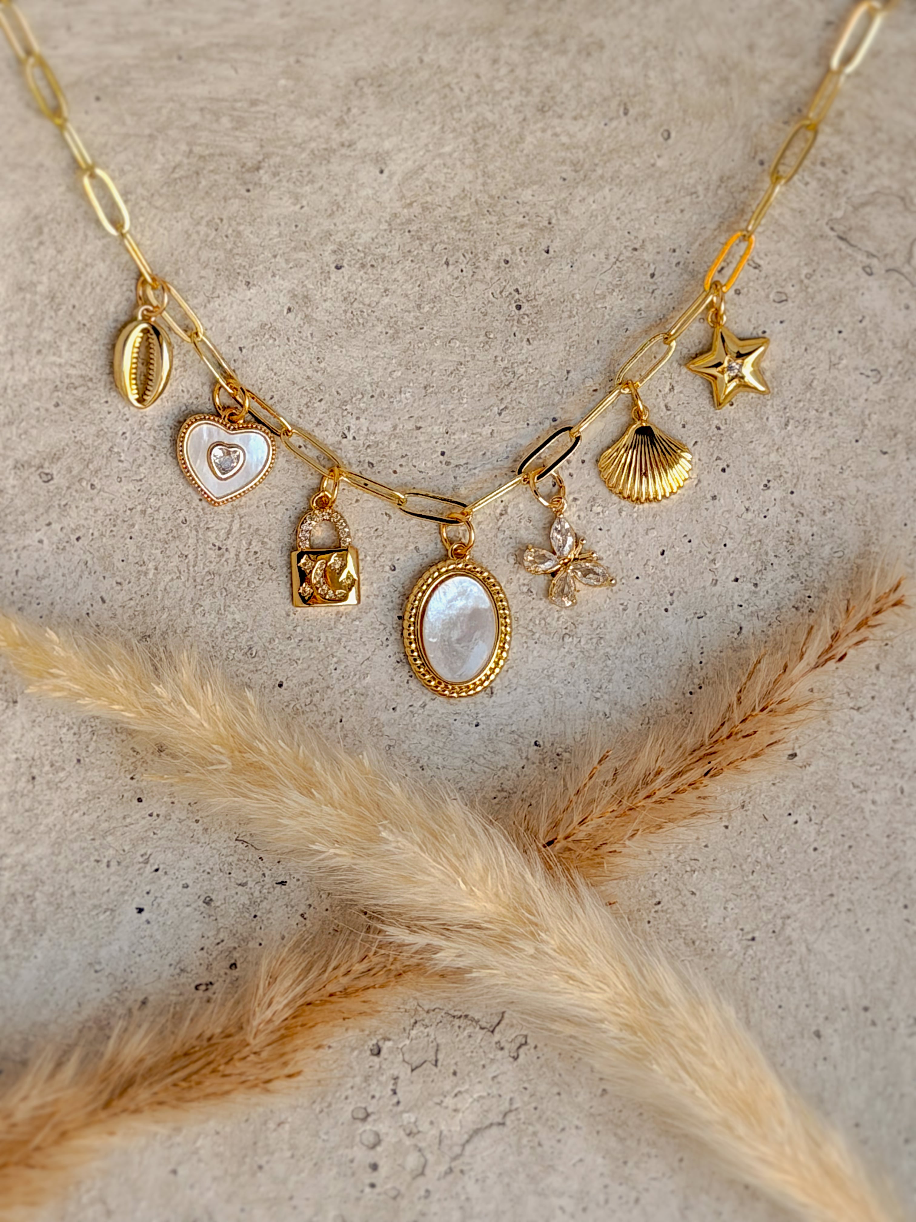 One of a Kind Mother of Pearl Charm Necklace with genuine mother of pearl pendant, freshwater pearls, cubic zirconia butterfly, heart, star, shell, lock, and cowrie shell charms on a 20-inch gold paperclip chain handcrafted by Rising Soul Jewelry.