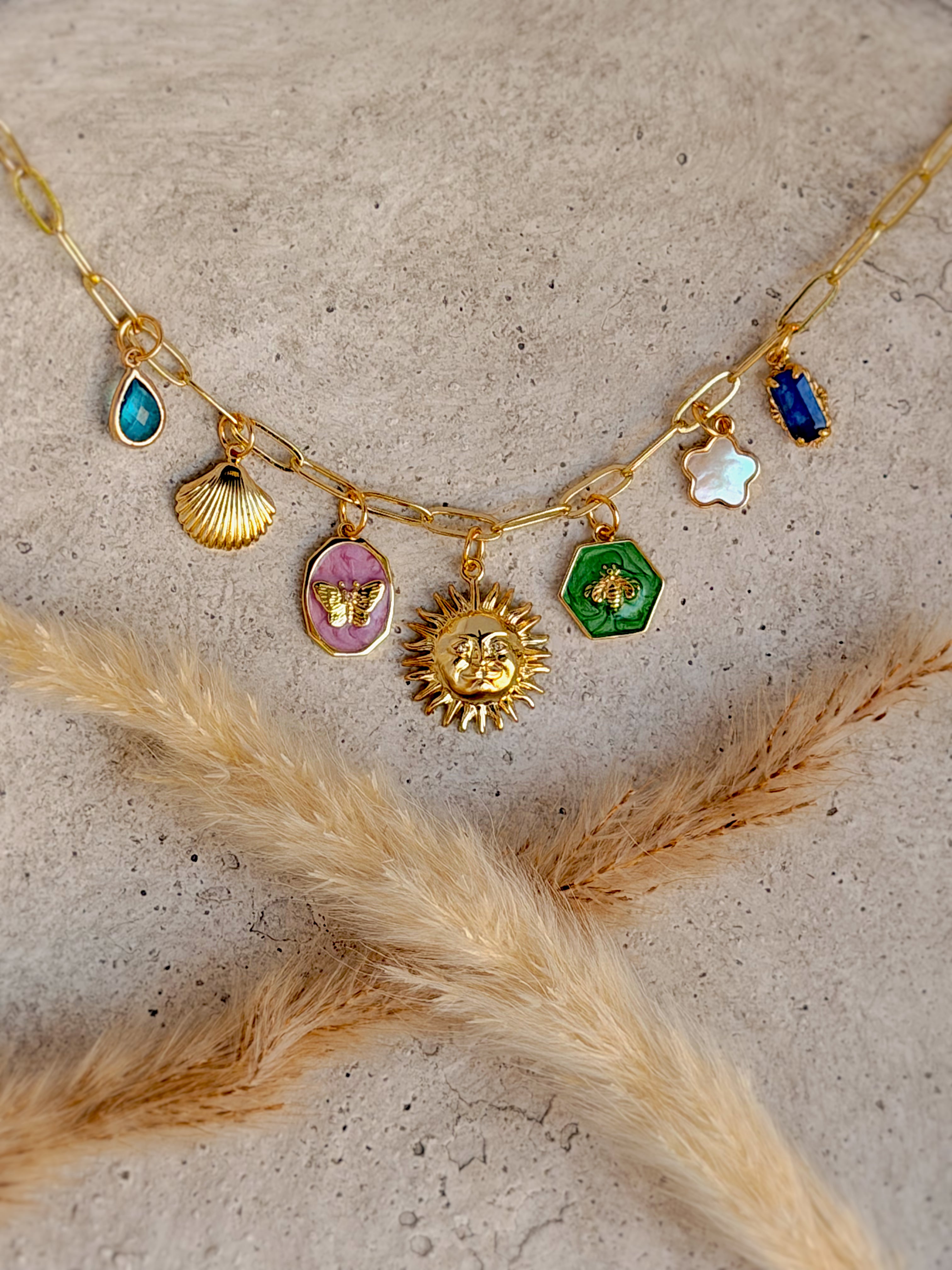 One of a Kind Sun Charm Necklace with genuine mother of pearl, colorful enamel butterfly and bee charms, cubic zirconia details, shell charm, and gold paperclip chain handcrafted by Rising Soul Jewelry.