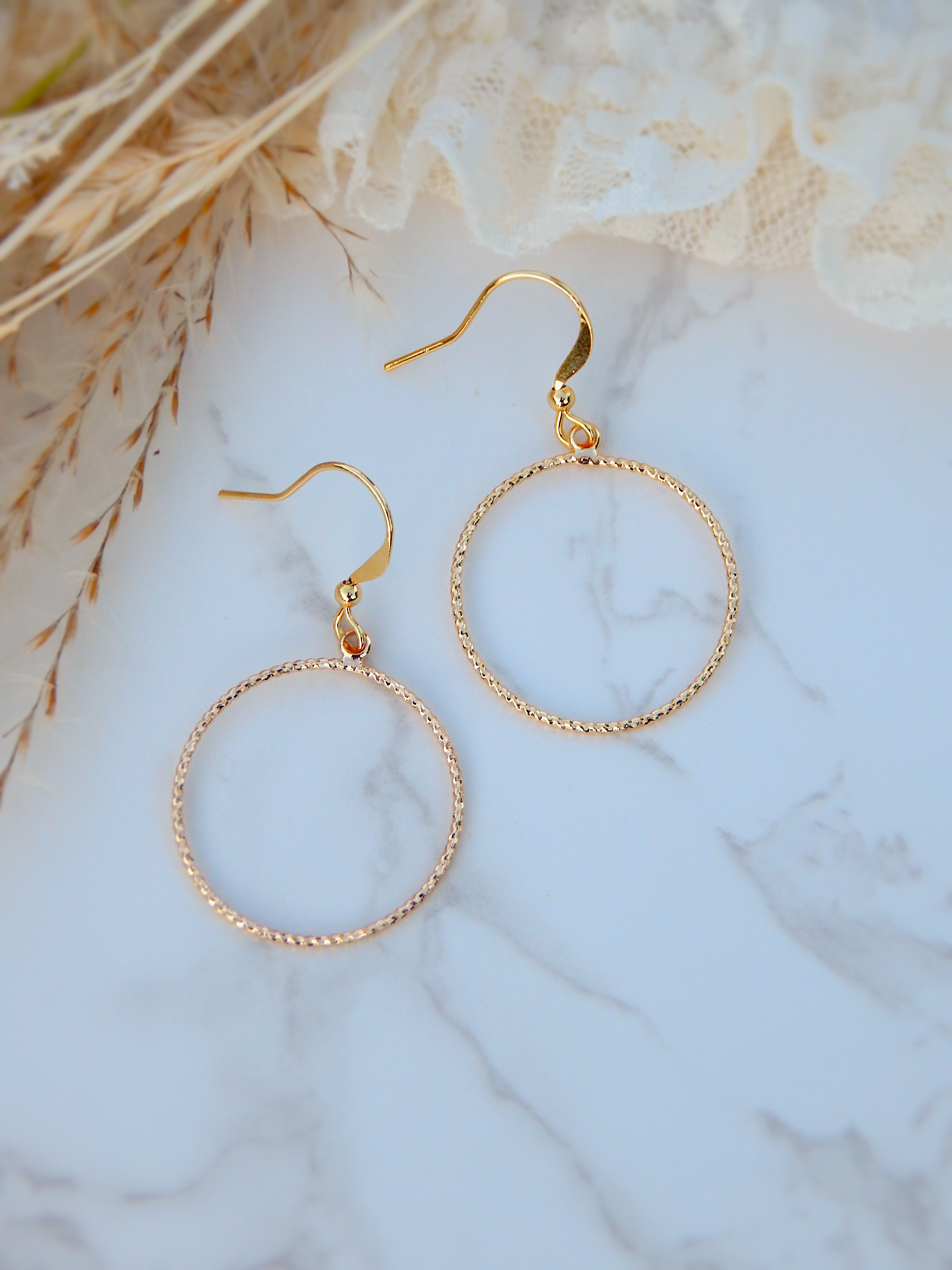 Gold textured circle hoop earrings on marble surface with soft neutral styling, minimalist boho jewelry