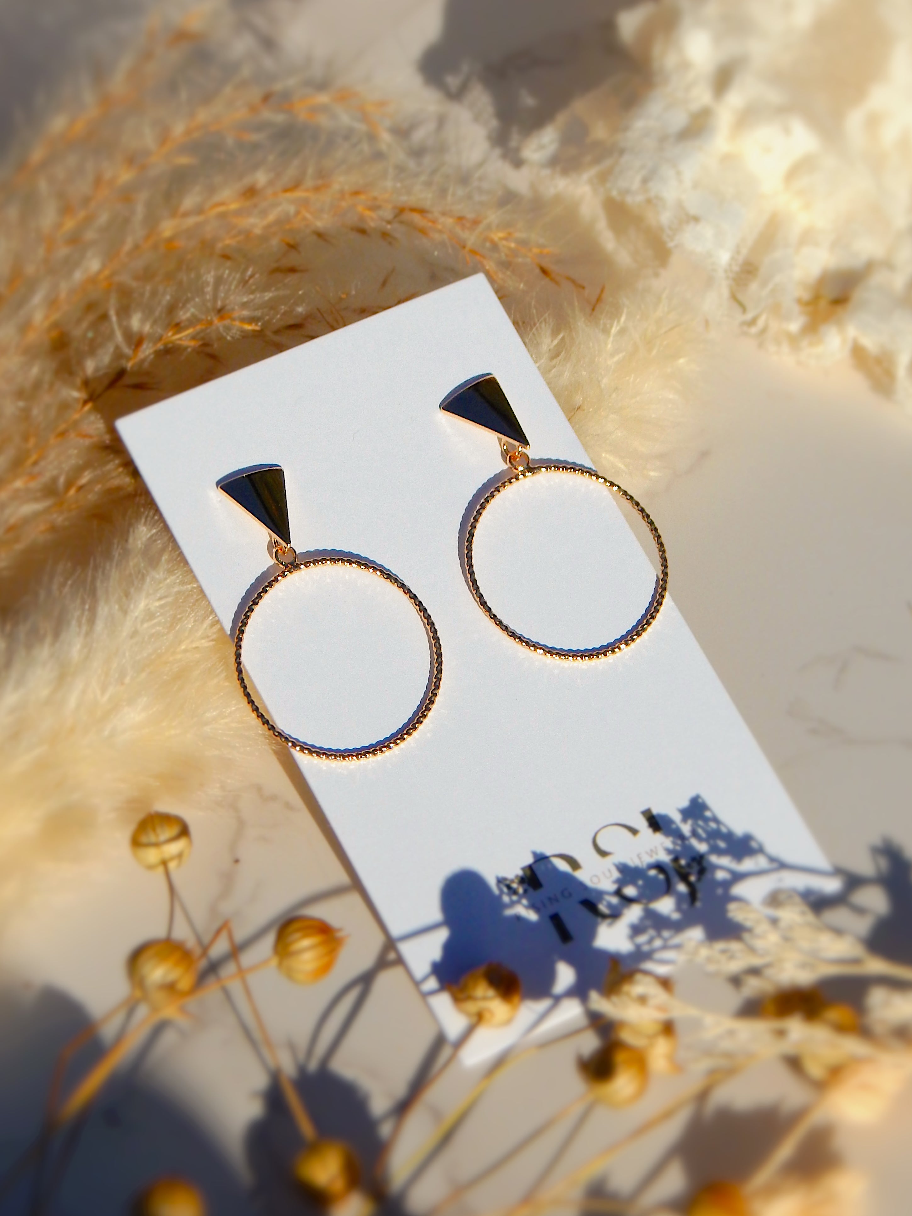 Gold triangle stud hoop earrings displayed on jewelry card with warm natural lighting