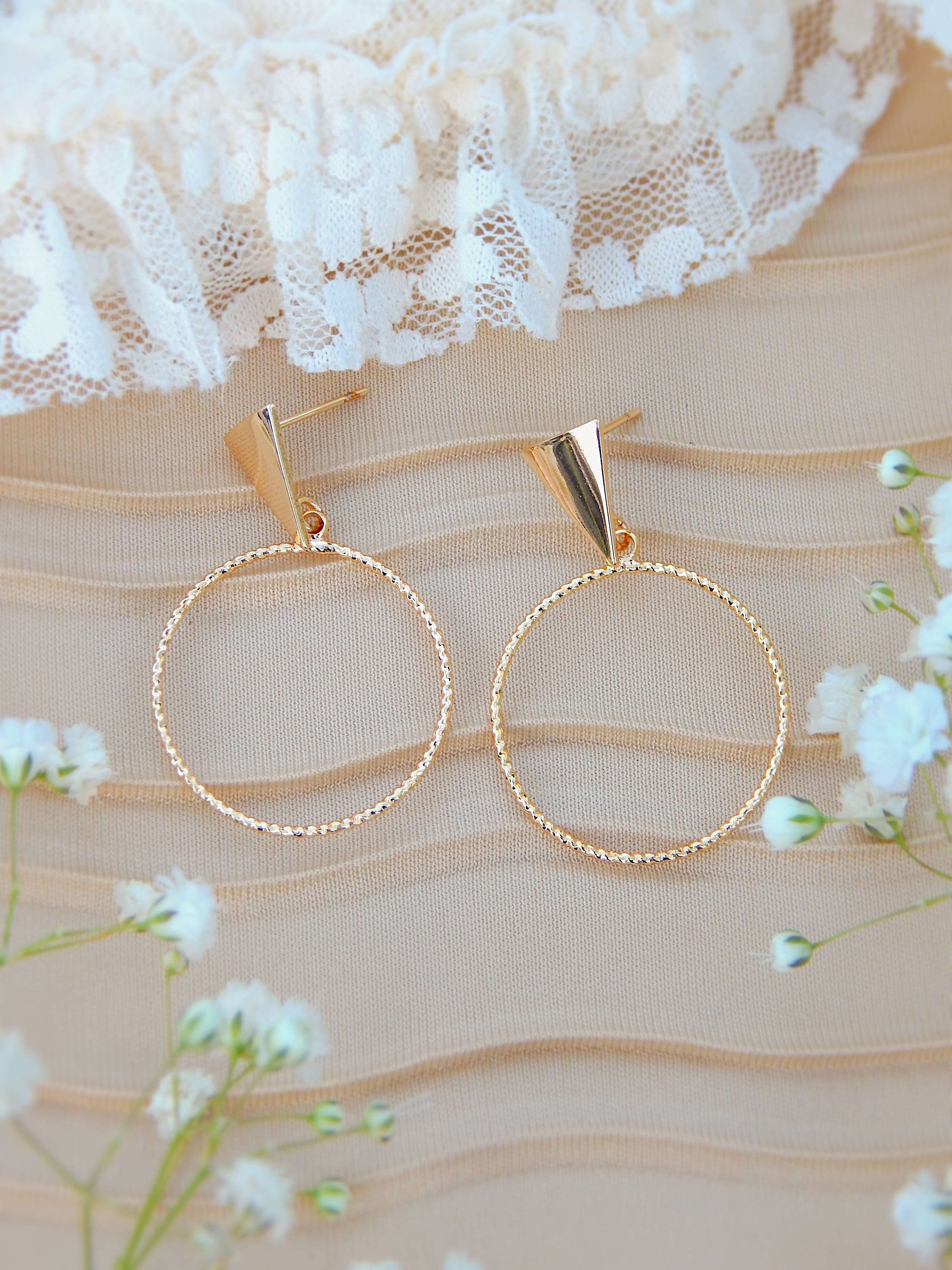 Gold triangle stud hoop earrings with textured circle design on neutral fabric background