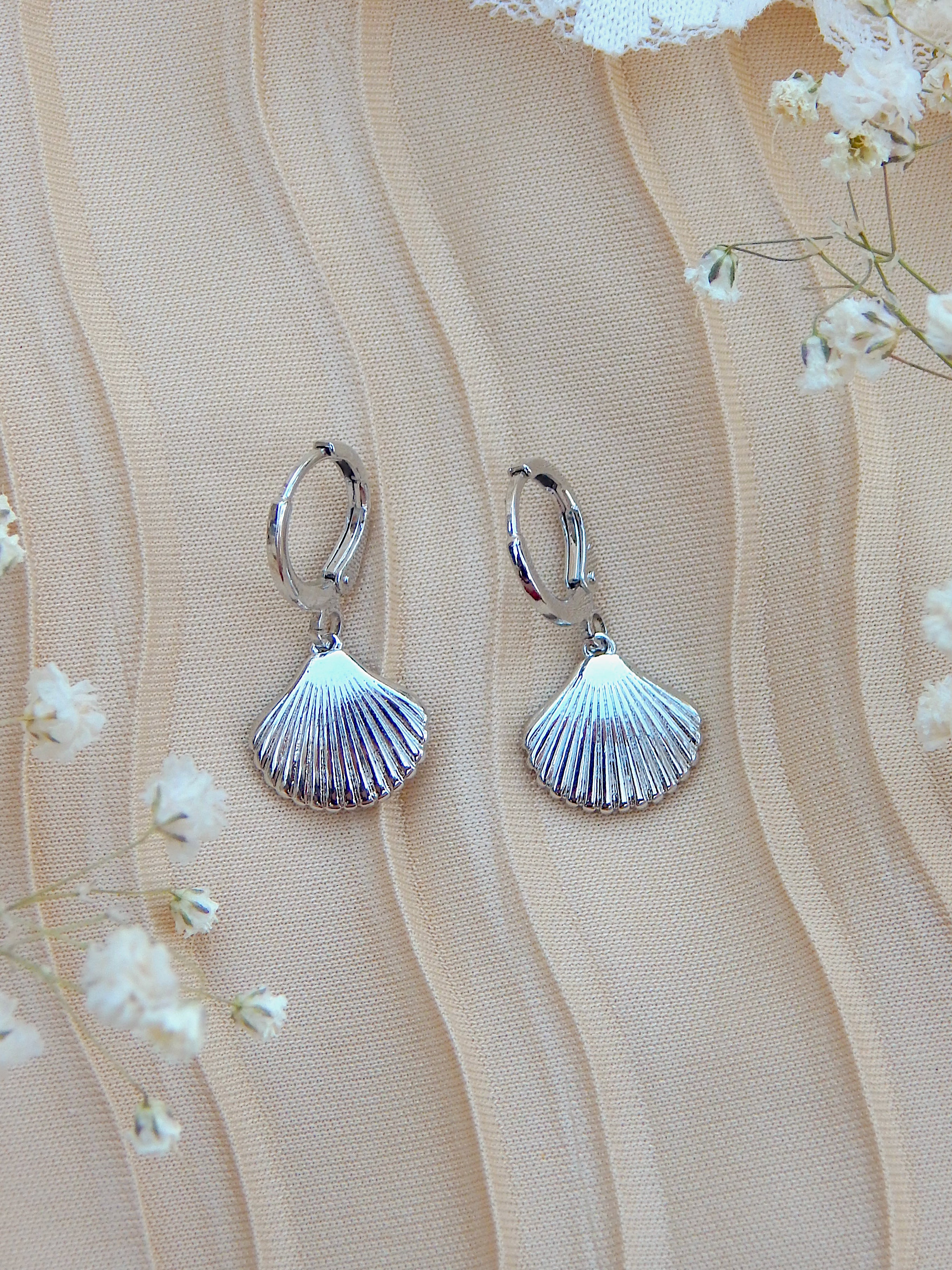 Silver seashell huggie earrings with shell charm on neutral background, minimal coastal jewelry design