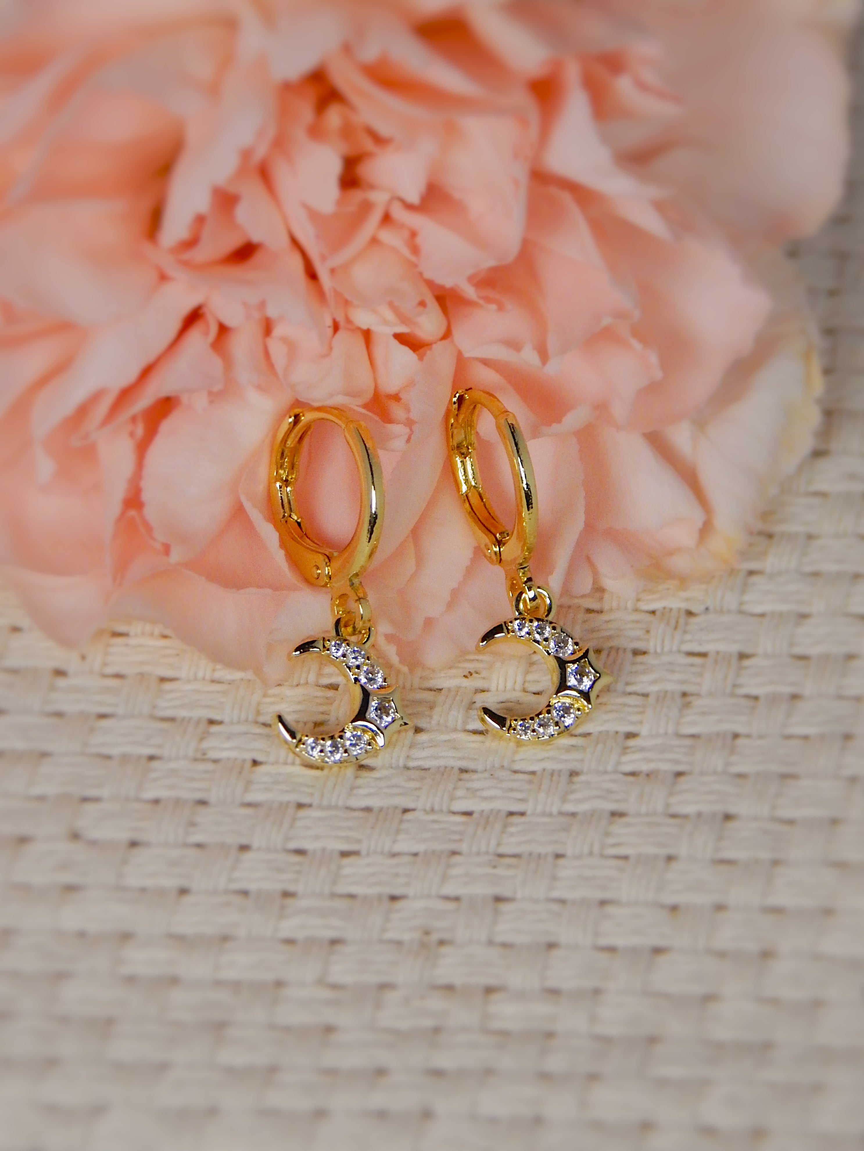 Gold huggie earrings with circular drop design on neutral background